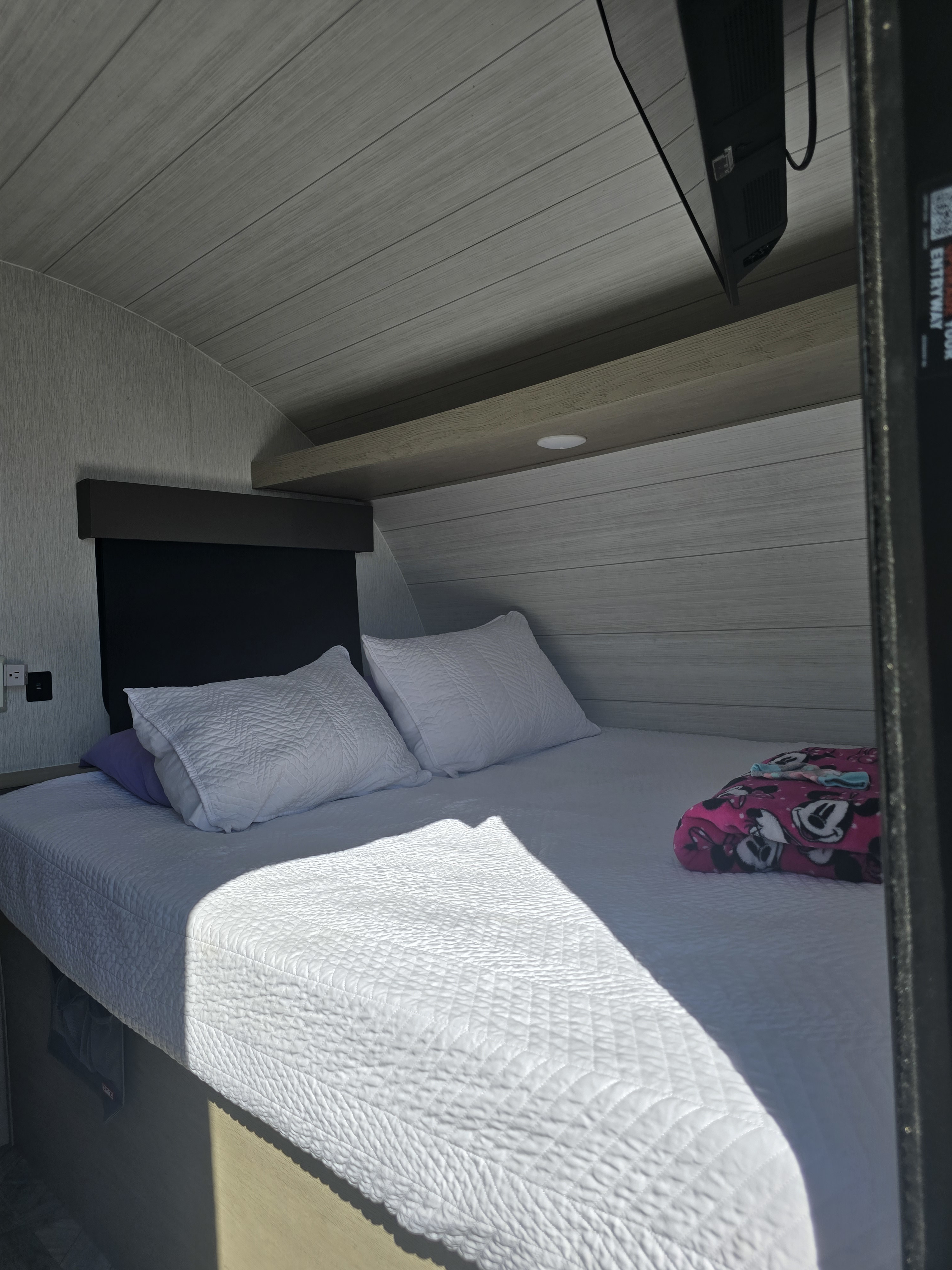 Inside a cozy RV rental bedroom: a comfortable bed with white quilted bedding, pillows, and a Minnie Mouse blanket.. Forest River Salem Cruise Lite 2024