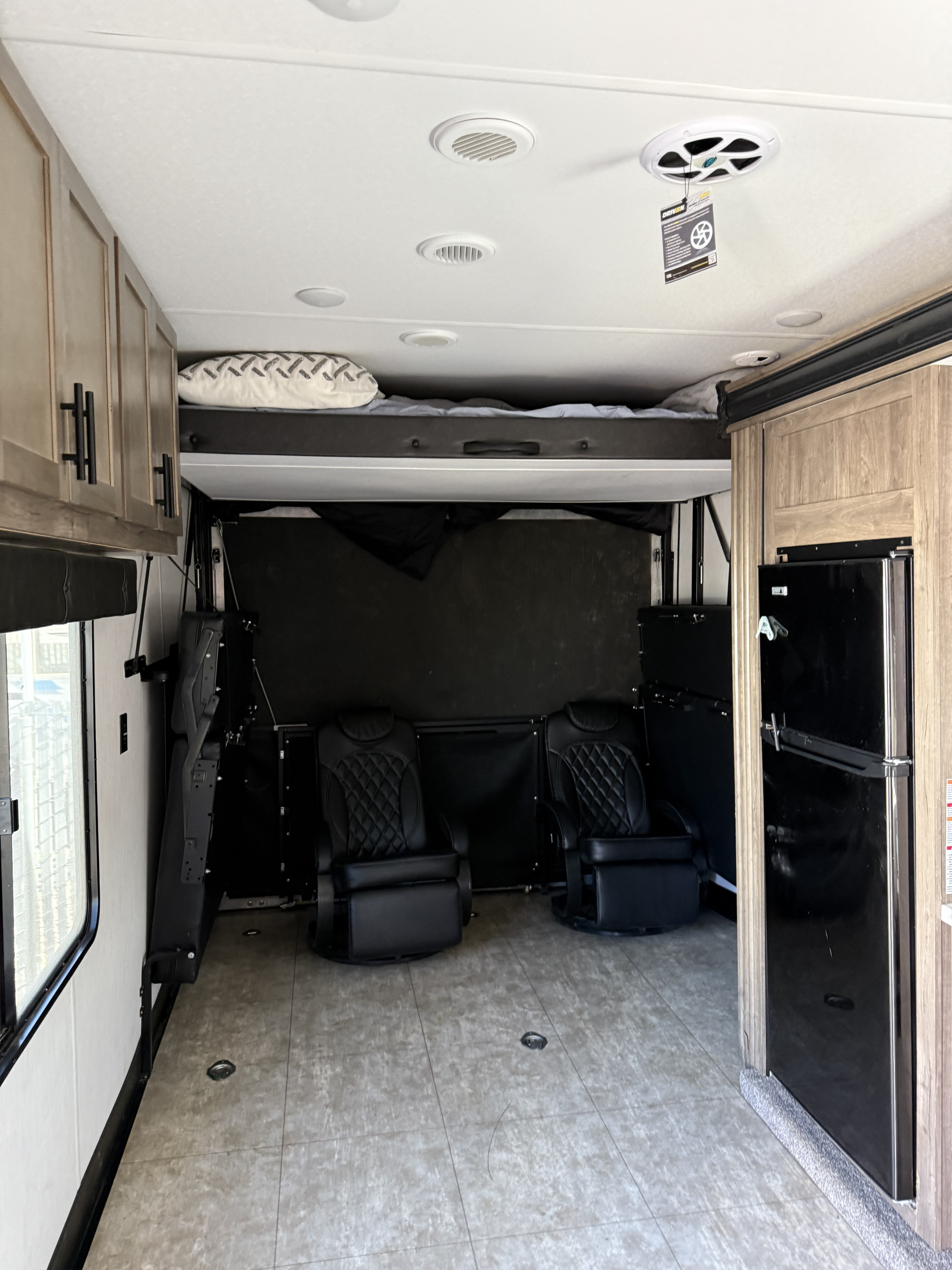 Inside this **rv rental**: A versatile toy hauler space with a bunk bed, two reclining chairs, and a large refrigerator.. Forest River Vengeance 2022