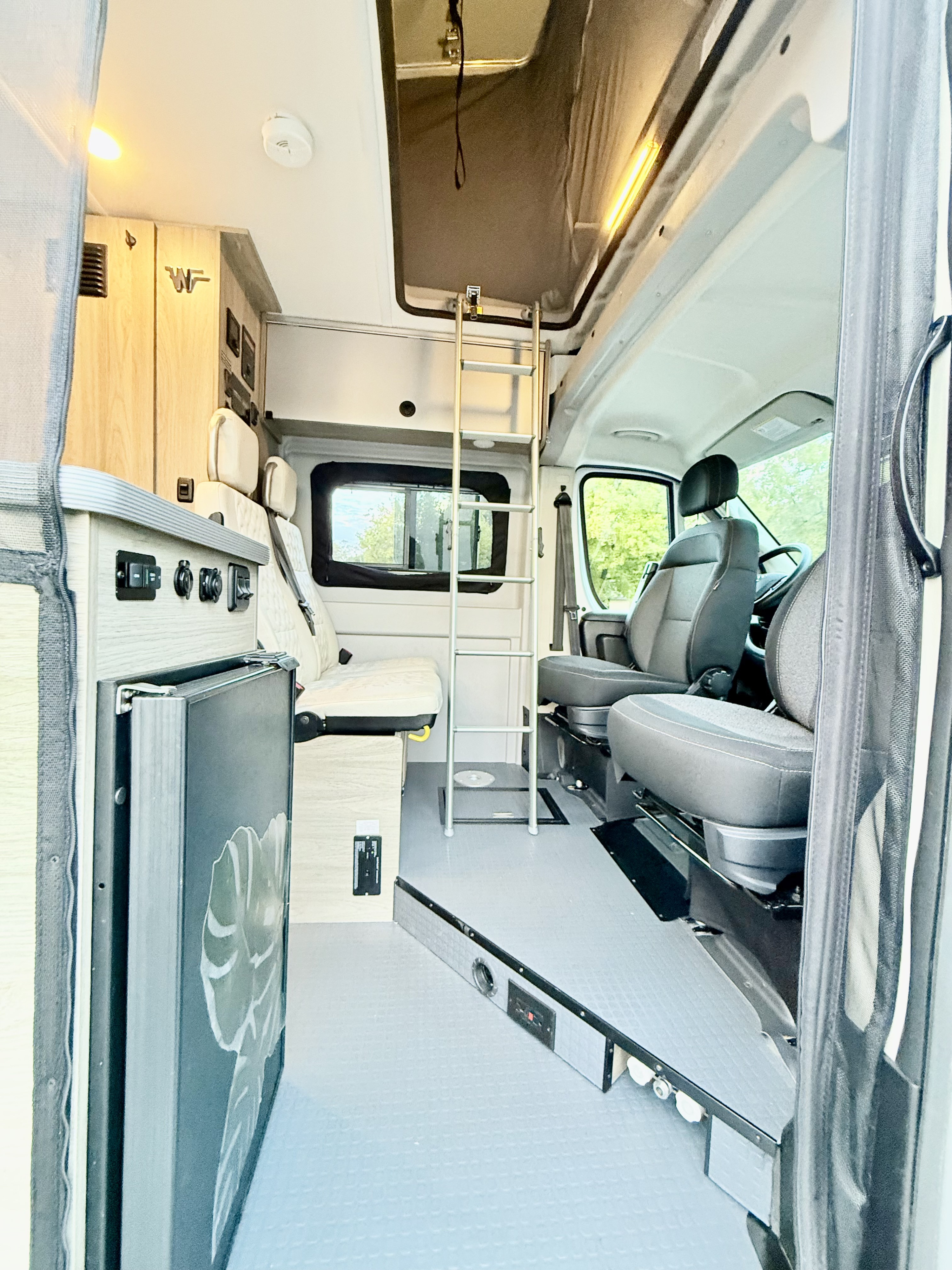Explore this bright RV rental camper van interior: pop-top access via ladder, kitchenette, and comfortable front seats.. Winnebago Solis 2022