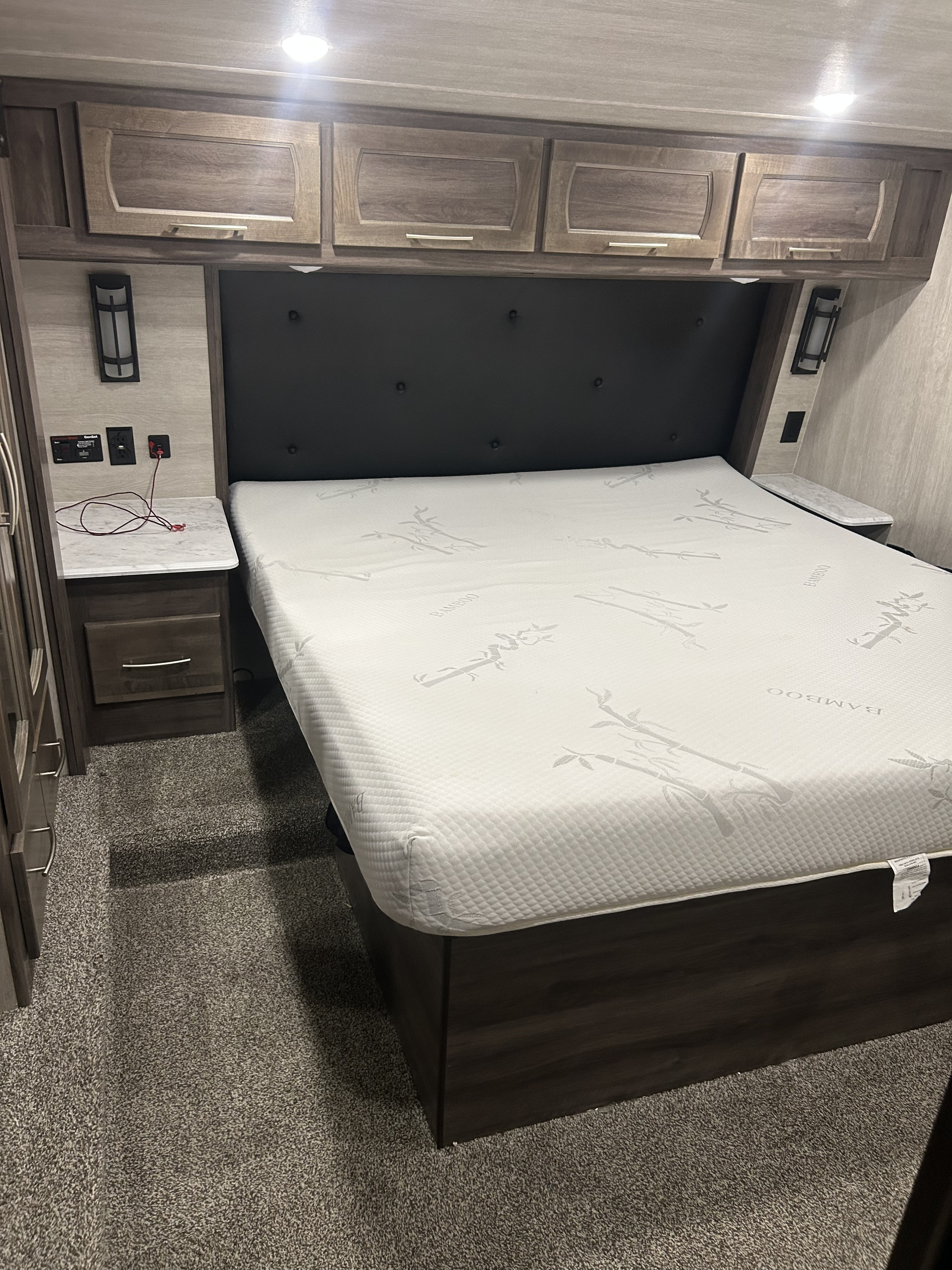 RV rental master bedroom with a comfortable bed, bamboo mattress, overhead cabinets, and built-in nightstands.. Genesis Supreme Rv Genesis Supreme 2023