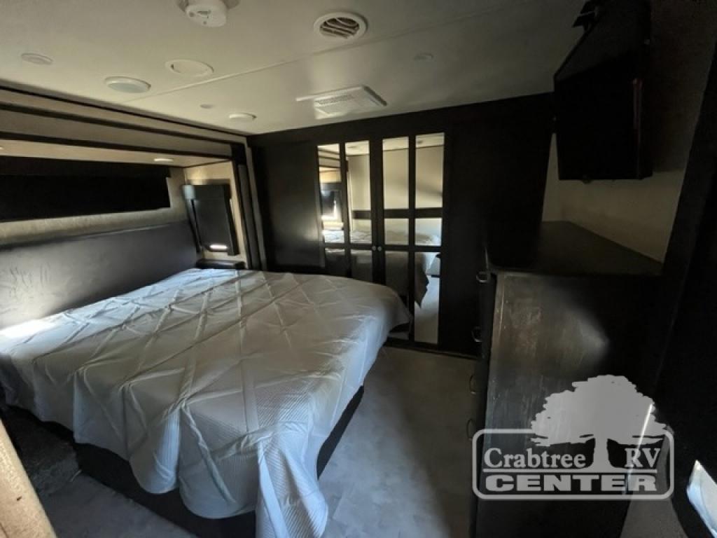Relax in this comfortable RV rental bedroom, featuring a large bed, TV, dresser, and mirrored closet for your travels.. Grand Design Momentum 2015