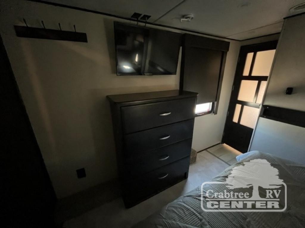 RV rental bedroom interior: dark dresser, TVs, and a bed with striped bedding. Features a window, door, and coat rack.. Grand Design Momentum 2015
