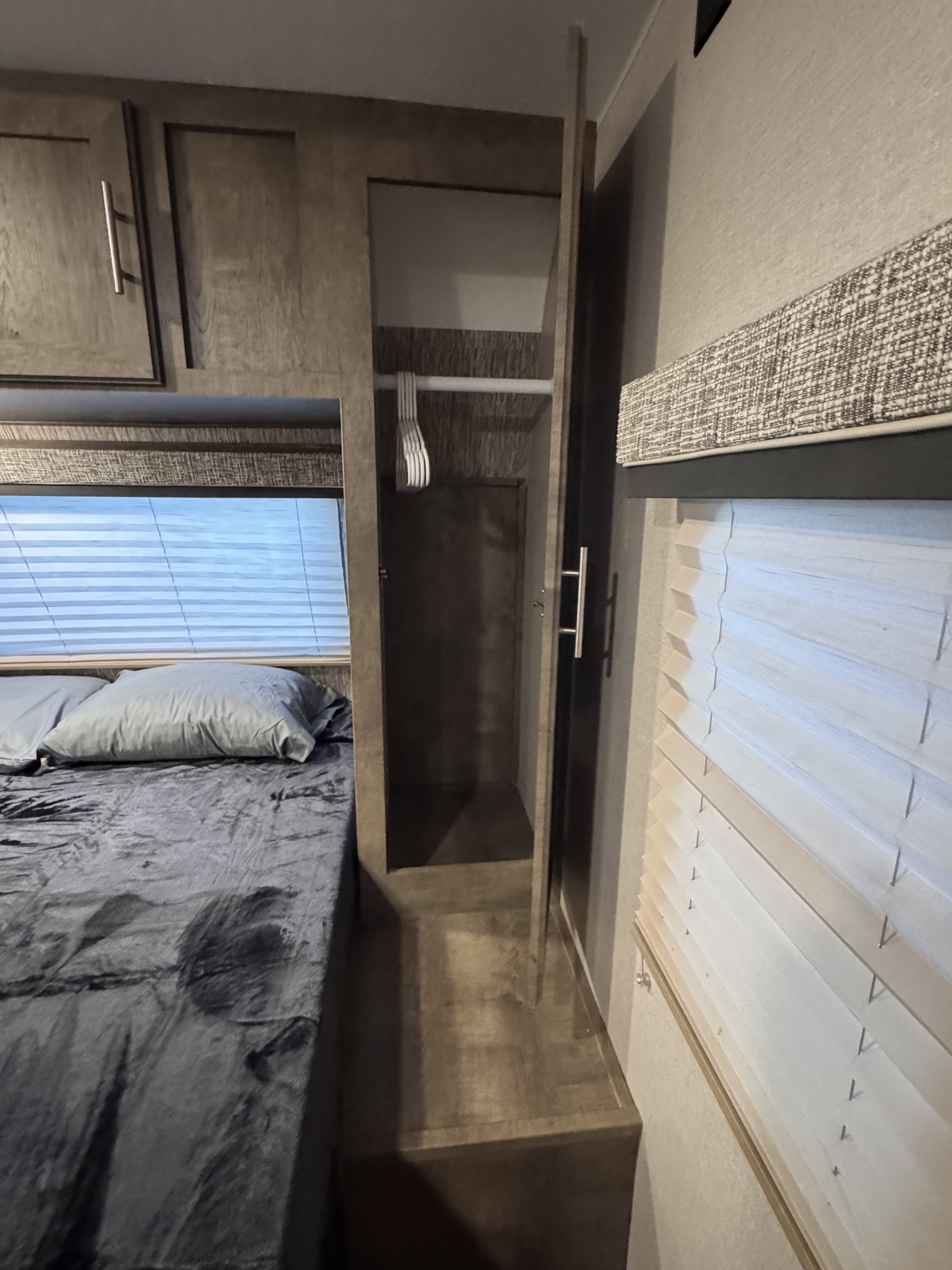 RV rental bedroom featuring a comfortable bed, window with blinds, and a compact wardrobe with hangers for travel.. Cruiser RV Embrace 2021