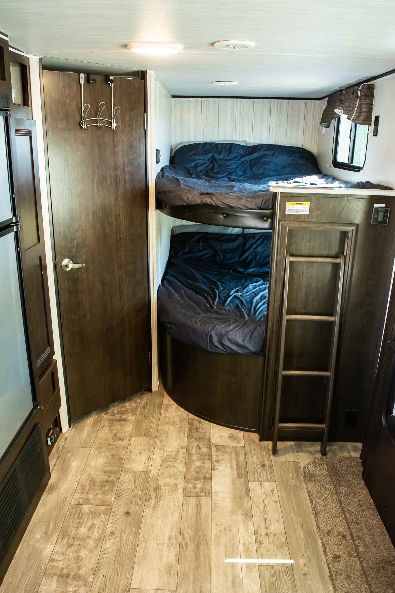 Cozy RV rental interior featuring dark wood bunk beds with a ladder, a closed door with hanging hooks, and wood-look flooring.. Heartland RVs Pioneer 2019