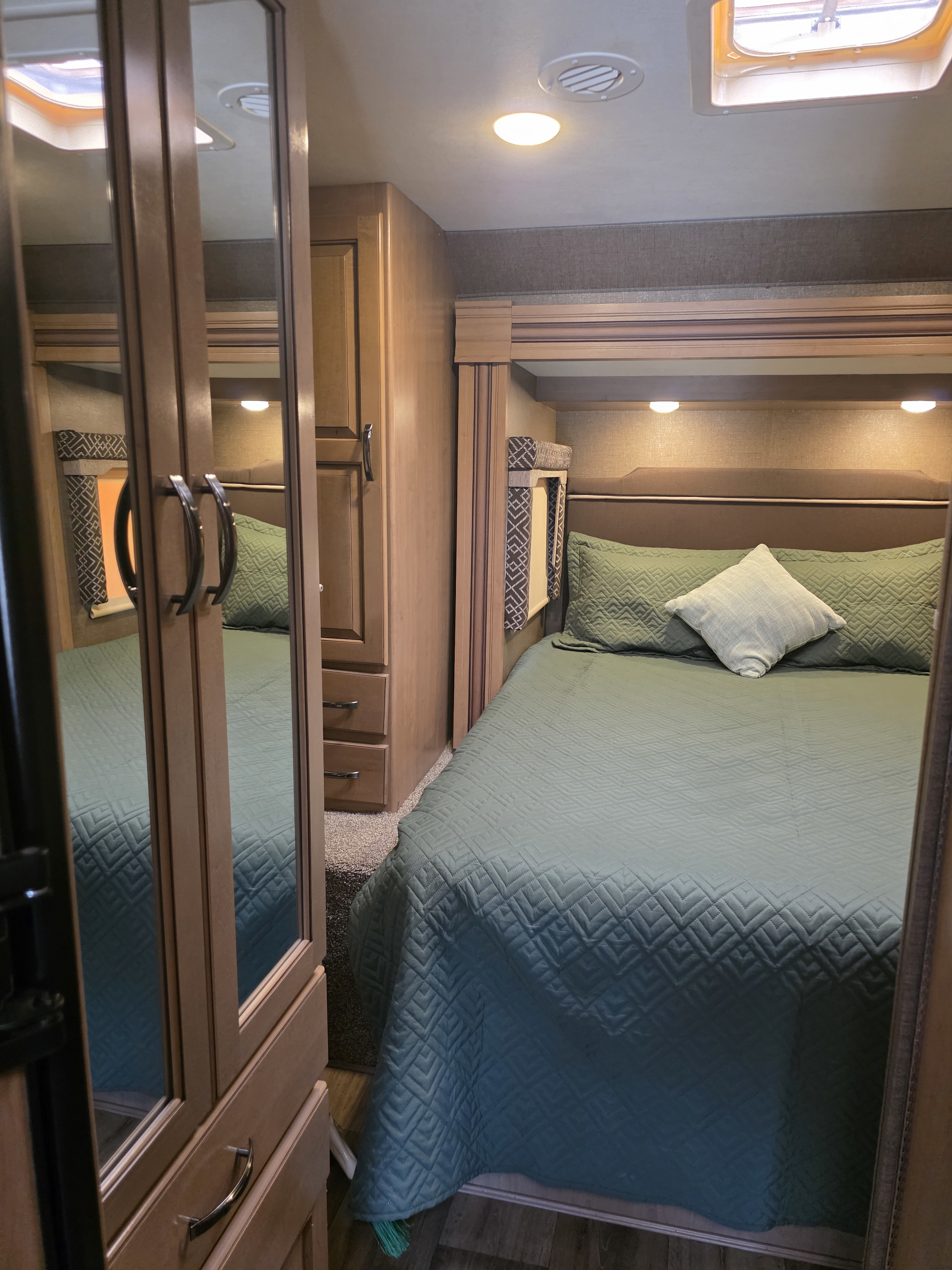Step into this cozy RV rental bedroom with a green-quilted bed, accent lighting, and mirrored wardrobe for your travels.. Thor Four Winds 2018