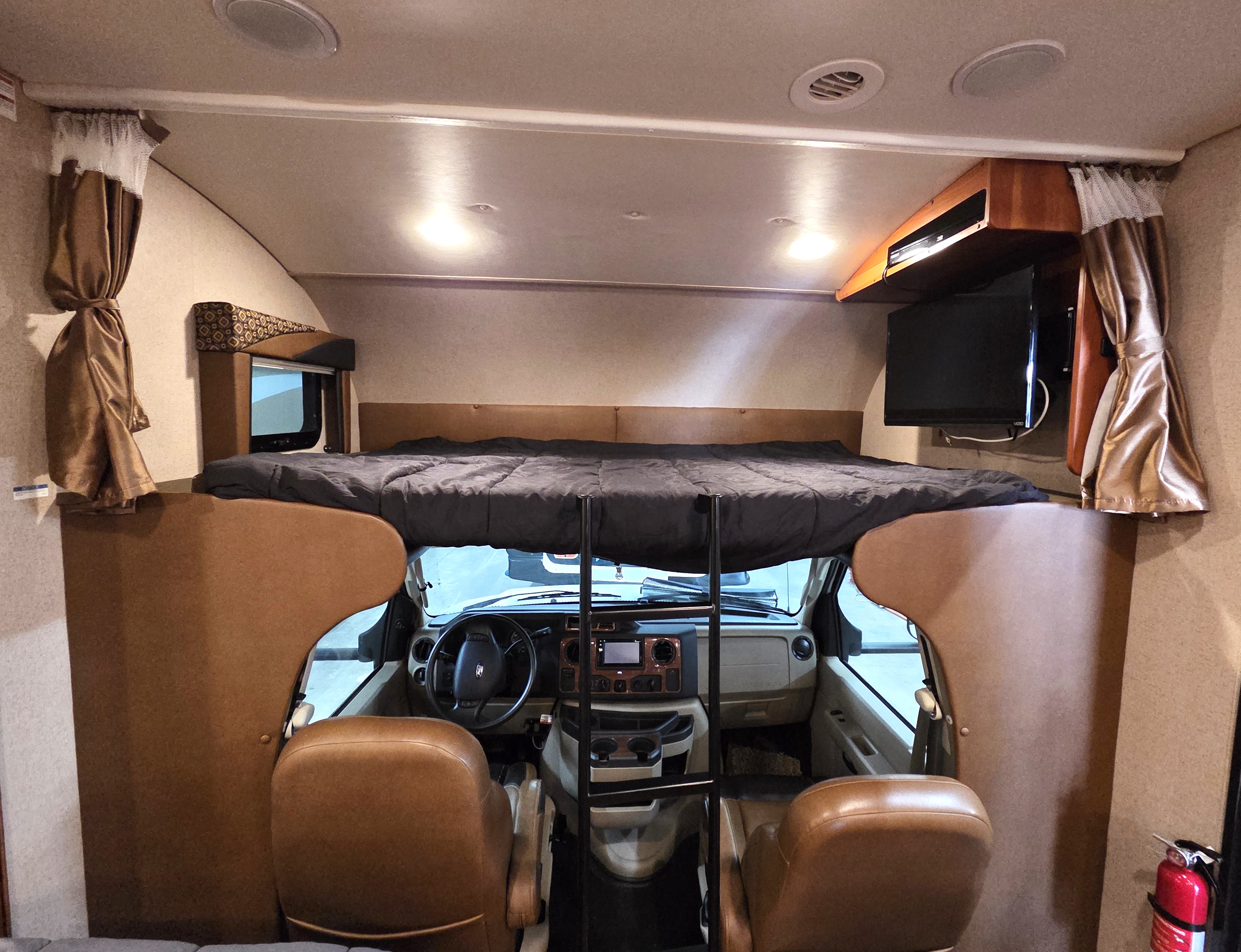 Interior of an RV rental motorhome: over-cab bed extends over the driver's cockpit and front seating area.. Jayco Greyhawk 2015