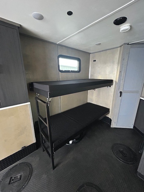 Cozy RV rental interior featuring a bunk bed setup, small window, and durable floor with access hatches. Ideal for travelers.. Team Lodge Extreme Toy Hauler 2022