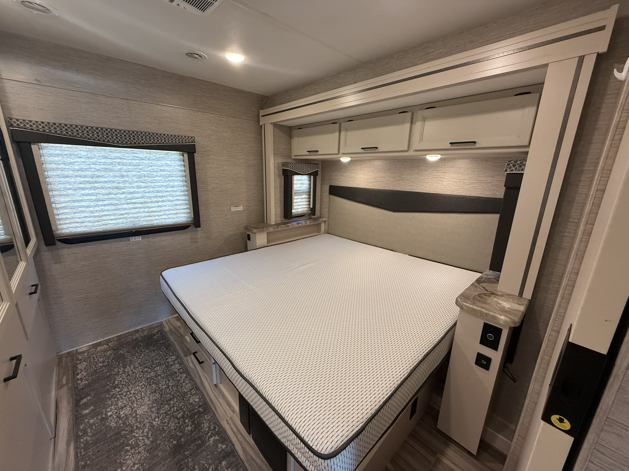 Modern RV rental bedroom featuring a large bed with under-bed storage, overhead cabinets, and a window with blinds.. Thor A.C.E. 2022