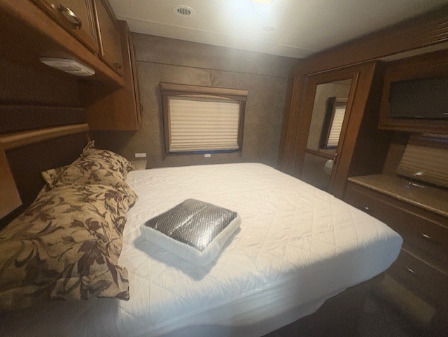 Inside an RV rental, a cozy bedroom with a large bed, built-in storage, and window blinds. Perfect for travel comfort.. A.C.E. A.C.E. Motorhome 2015