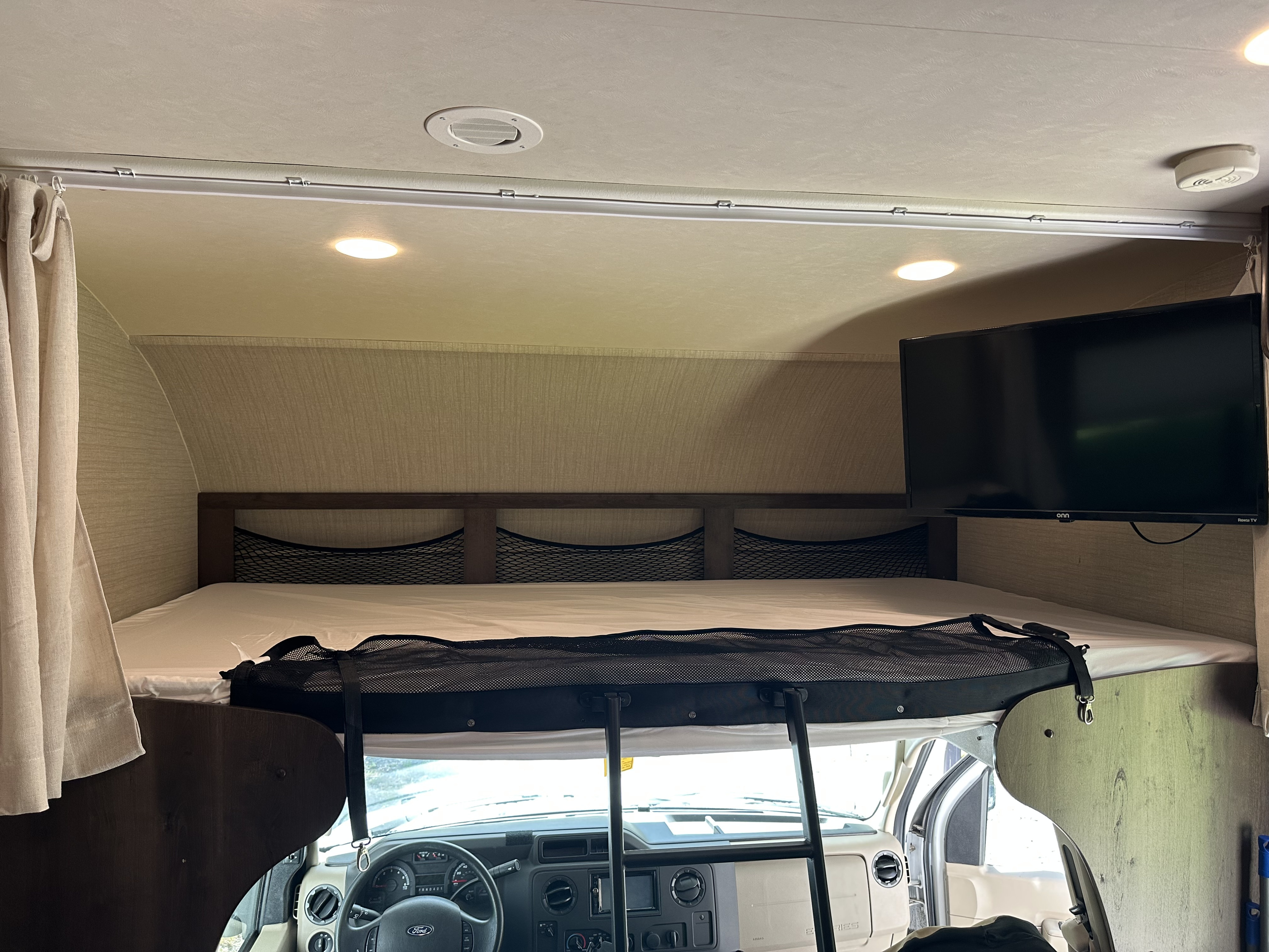 Inside this **rv rental**: View of the cab-over bed with safety net, mounted TV, and the dashboard below.. Jayco Redhawk 2018