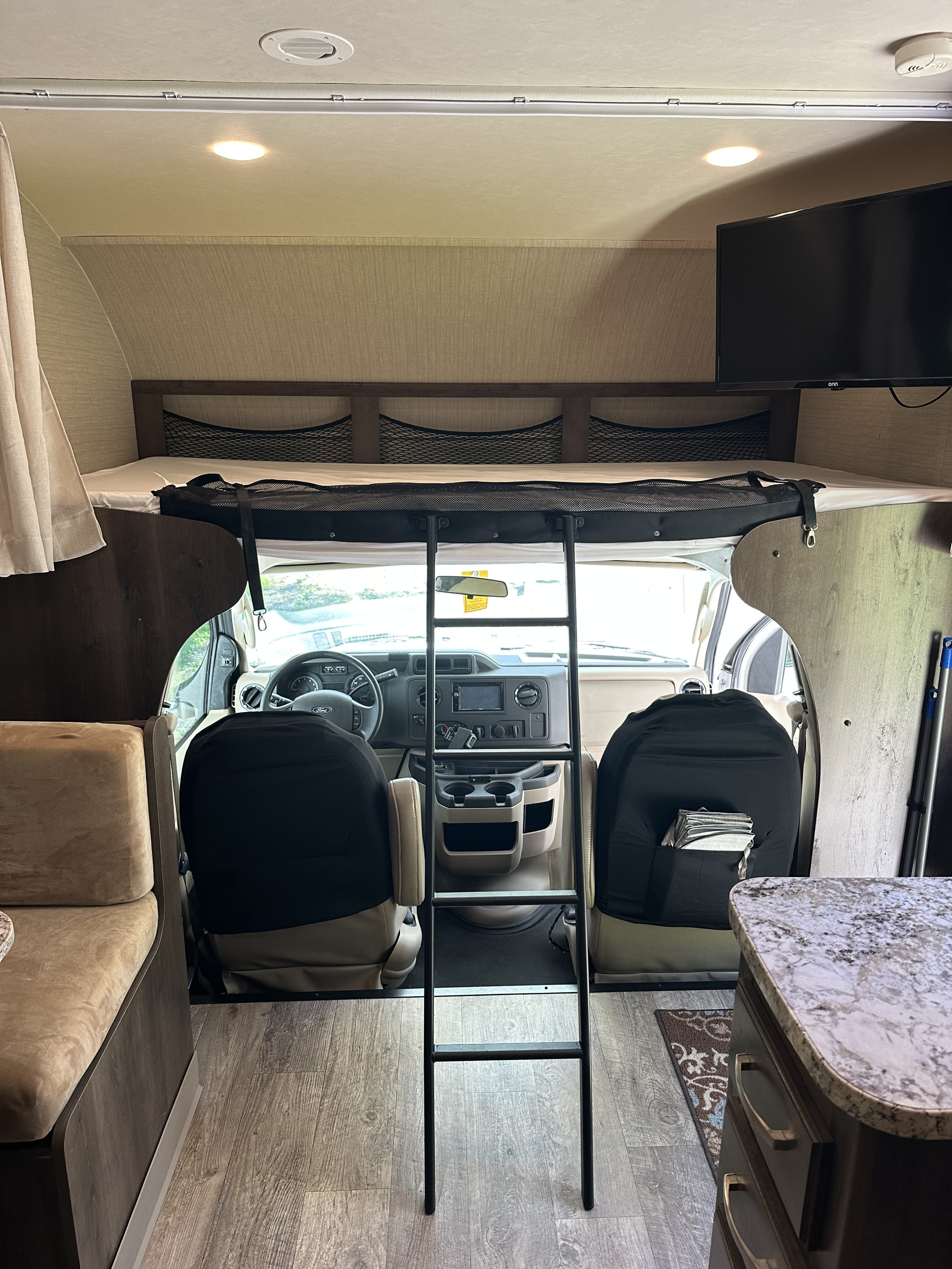 RV rental interior: over-cab bunk with ladder, driver's cockpit, dinette, and kitchen counter visible. A functional camper space.. Jayco Redhawk 2018