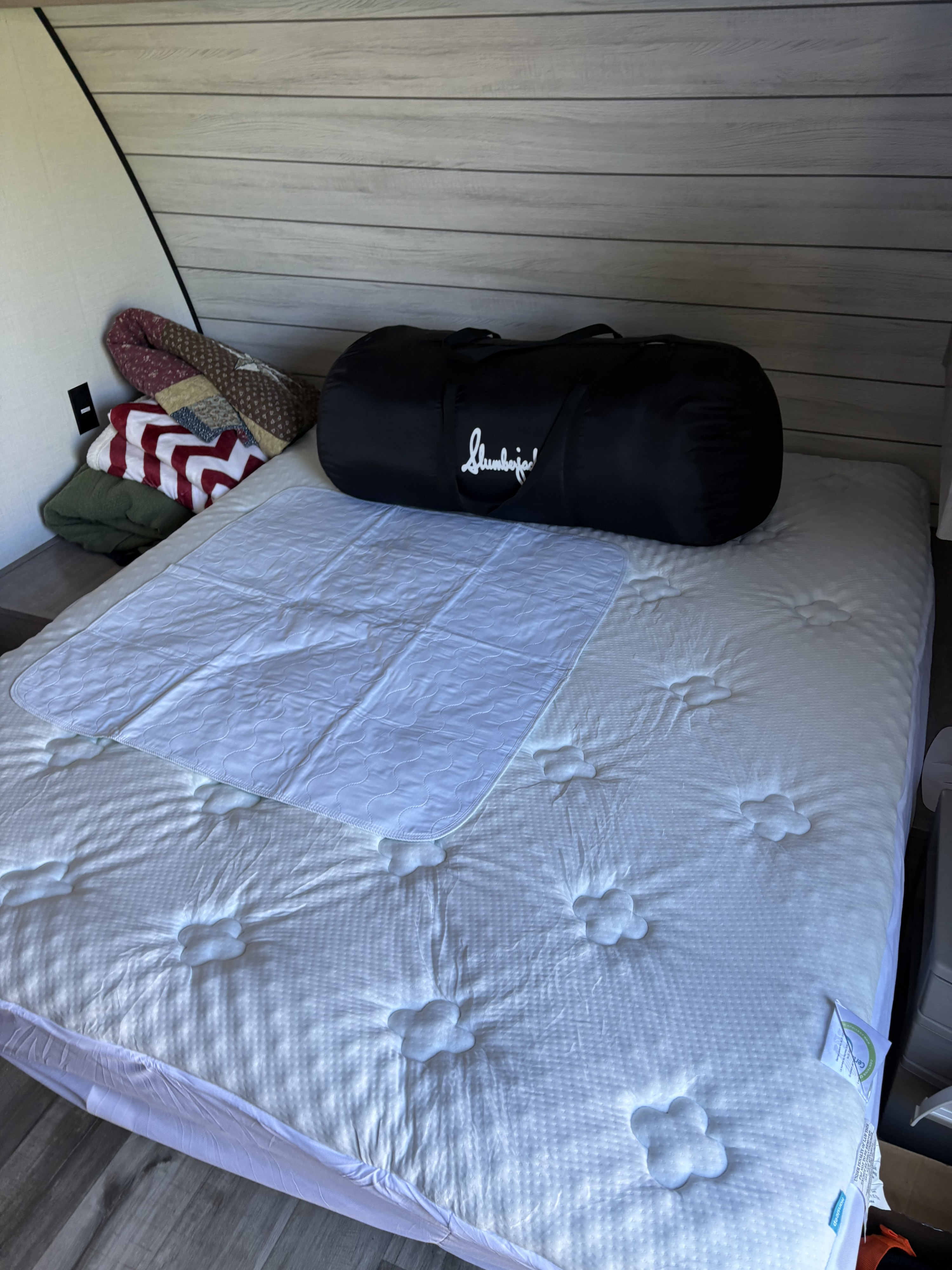 Setup for an RV rental: a plush mattress with a protector, folded blankets, and a Slumberjack bag in the bedroom.. Dutchmen Kodiak Cub 2024