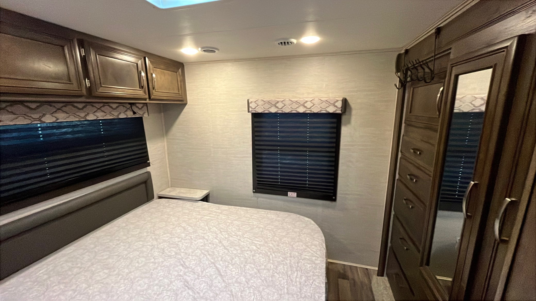 Comfortable RV rental bedroom featuring a bed, overhead cabinets, windows with blinds, and a mirrored closet.. Jayco Redhawk 2021