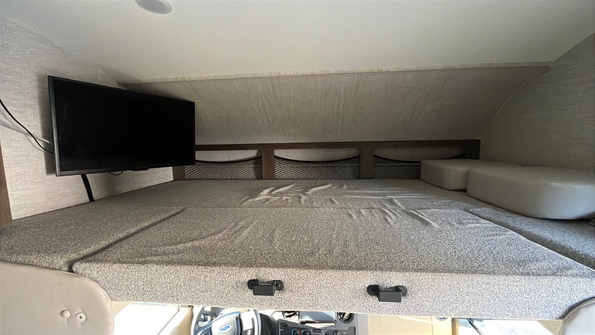 RV rental's cozy cab-over bunk bed features a TV mounted to the side and convenient storage nets above the mattress.. Jayco Redhawk 2021