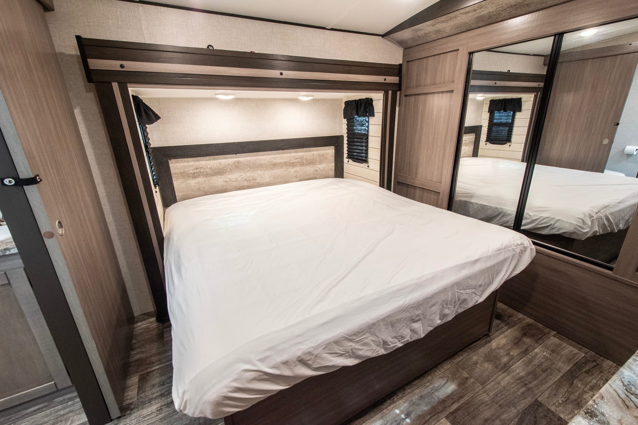 RV rental bedroom with a neatly made bed, built-in lighting, wood-look flooring, and mirrored closet doors.. Crossroads RV Sunset Trail 2022