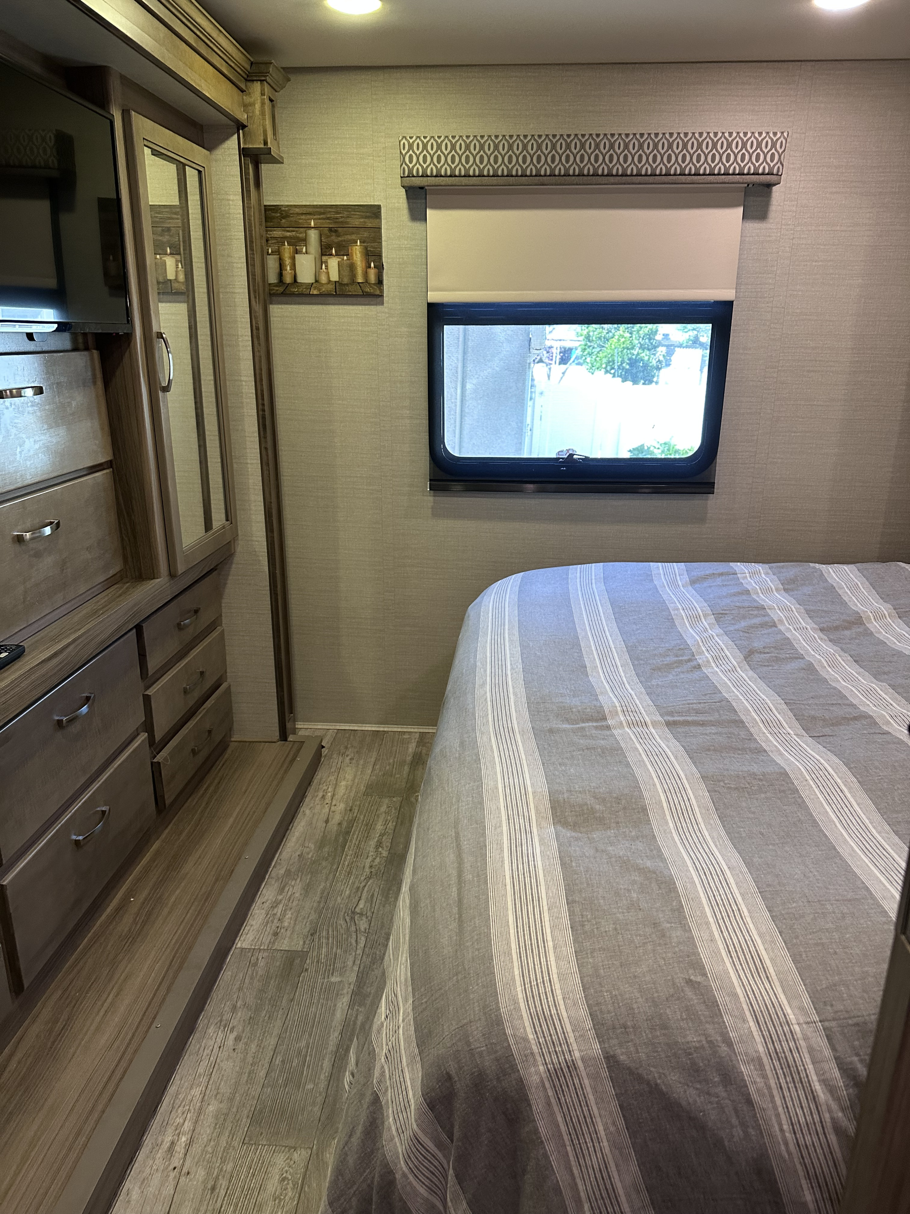 Cozy RV rental bedroom with striped bed, window, TV, mirrored closet, and wood-look flooring.. Jayco Precept 2018