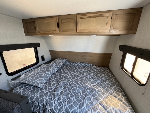 Cozy rv rental bedroom featuring a bed with patterned bedding, overhead cabinets, and windows, ideal for travel.. Cherokee WolfPup 2025