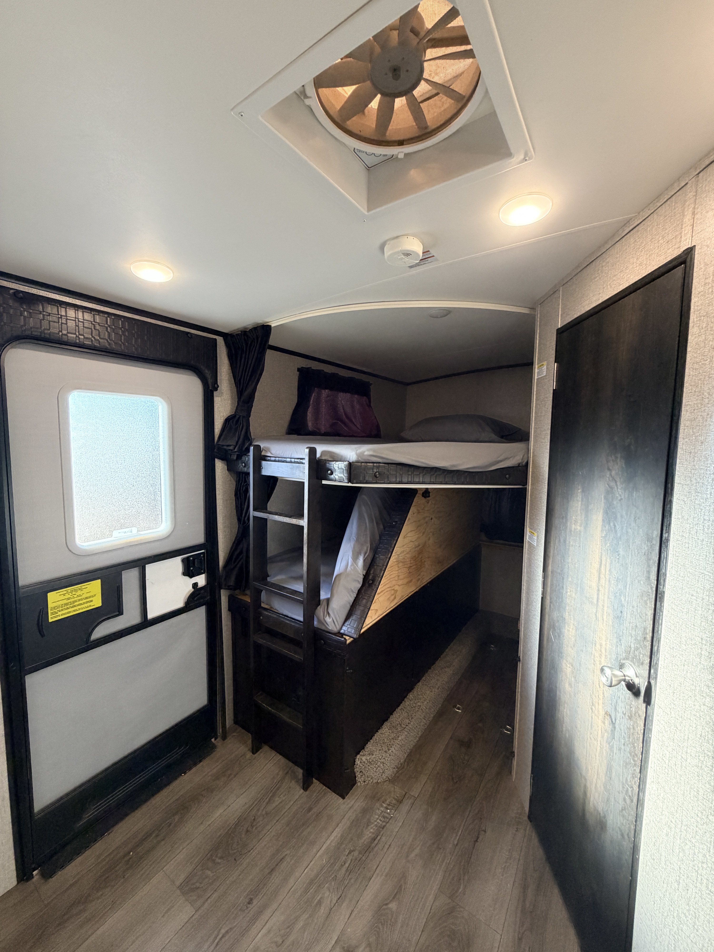 Inside an RV rental: Compact sleeping area with bunk beds, an entrance door, and a ceiling fan for ventilation.. Jayco White Hawk 2021