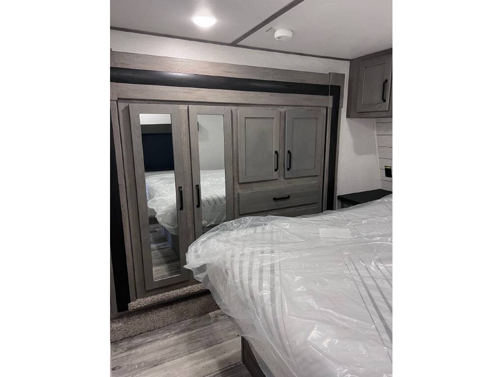 Modern RV rental bedroom: mirrored wardrobe, overhead storage, and a bed covered in plastic, ready for your trip.. Keystone RV Carbon Toy Hauler 2022