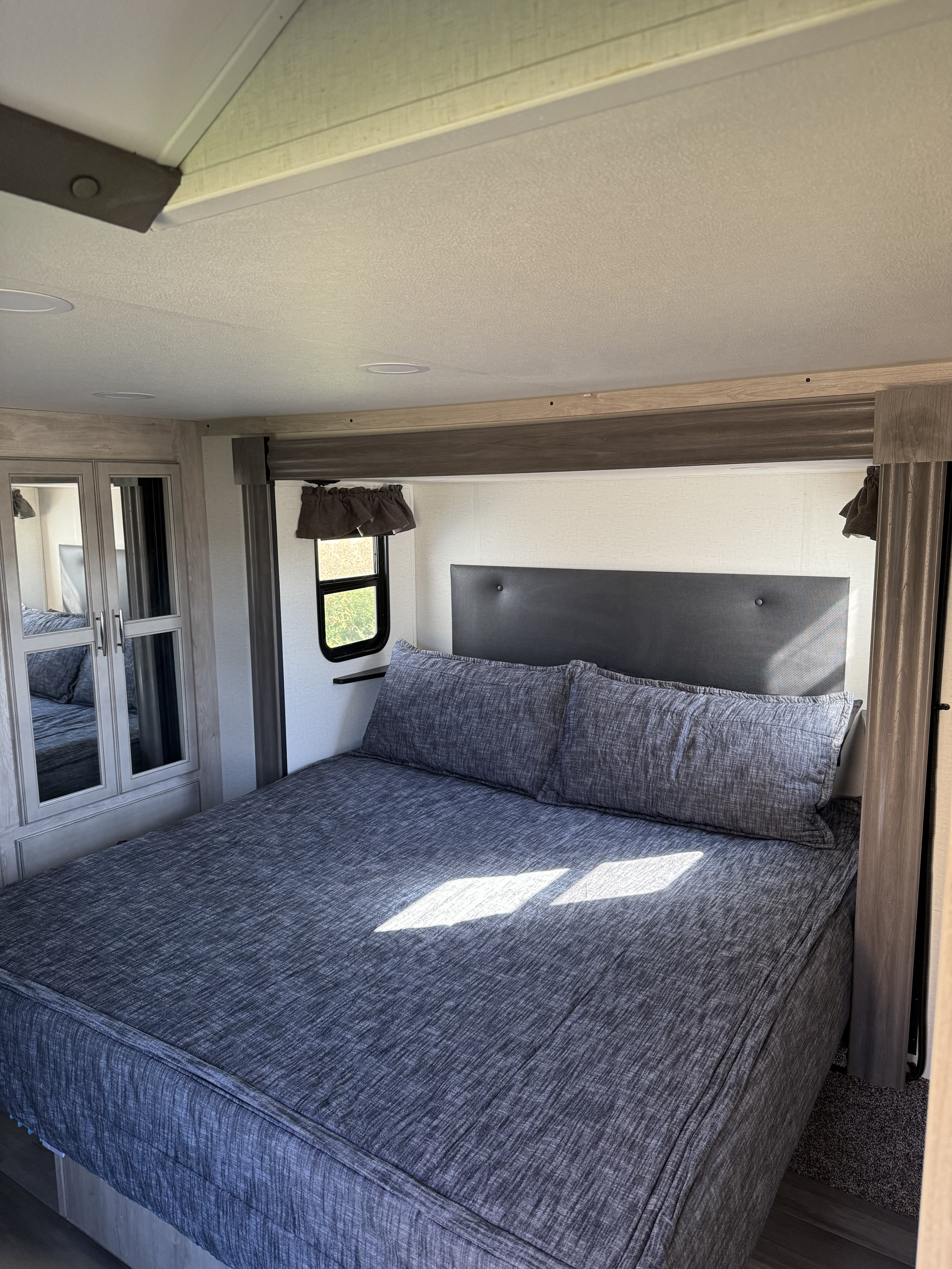 Comfortable RV rental bedroom with a spacious bed, grey bedding, and mirrored wardrobe. Ready for relaxation.. Forest River 4X4FSAS26RJ046944 2024