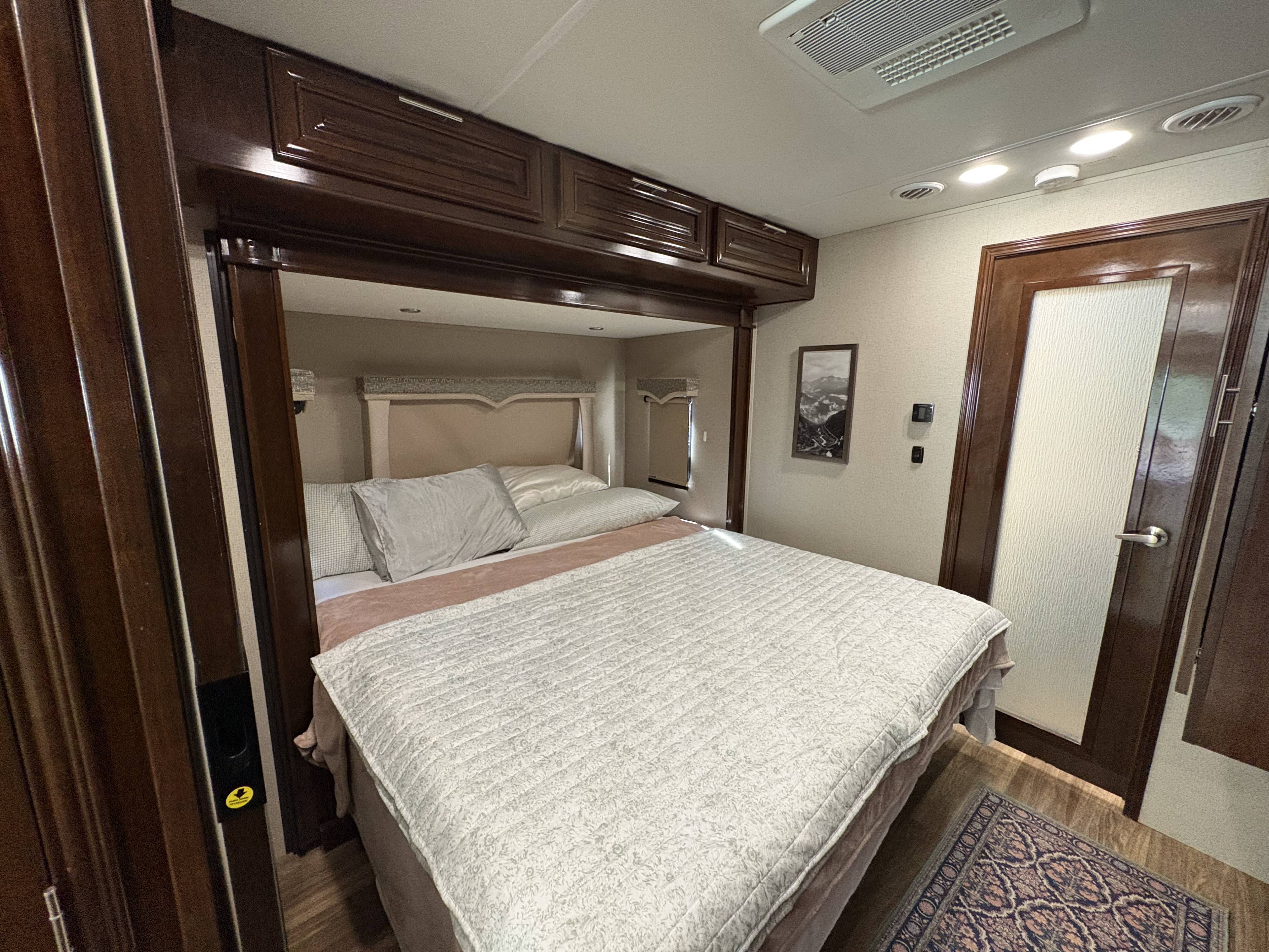 Comfortable RV rental bedroom featuring a queen bed, dark wood cabinets, modern lighting, and a small rug for a cozy feel.. Georgetown XL 2019