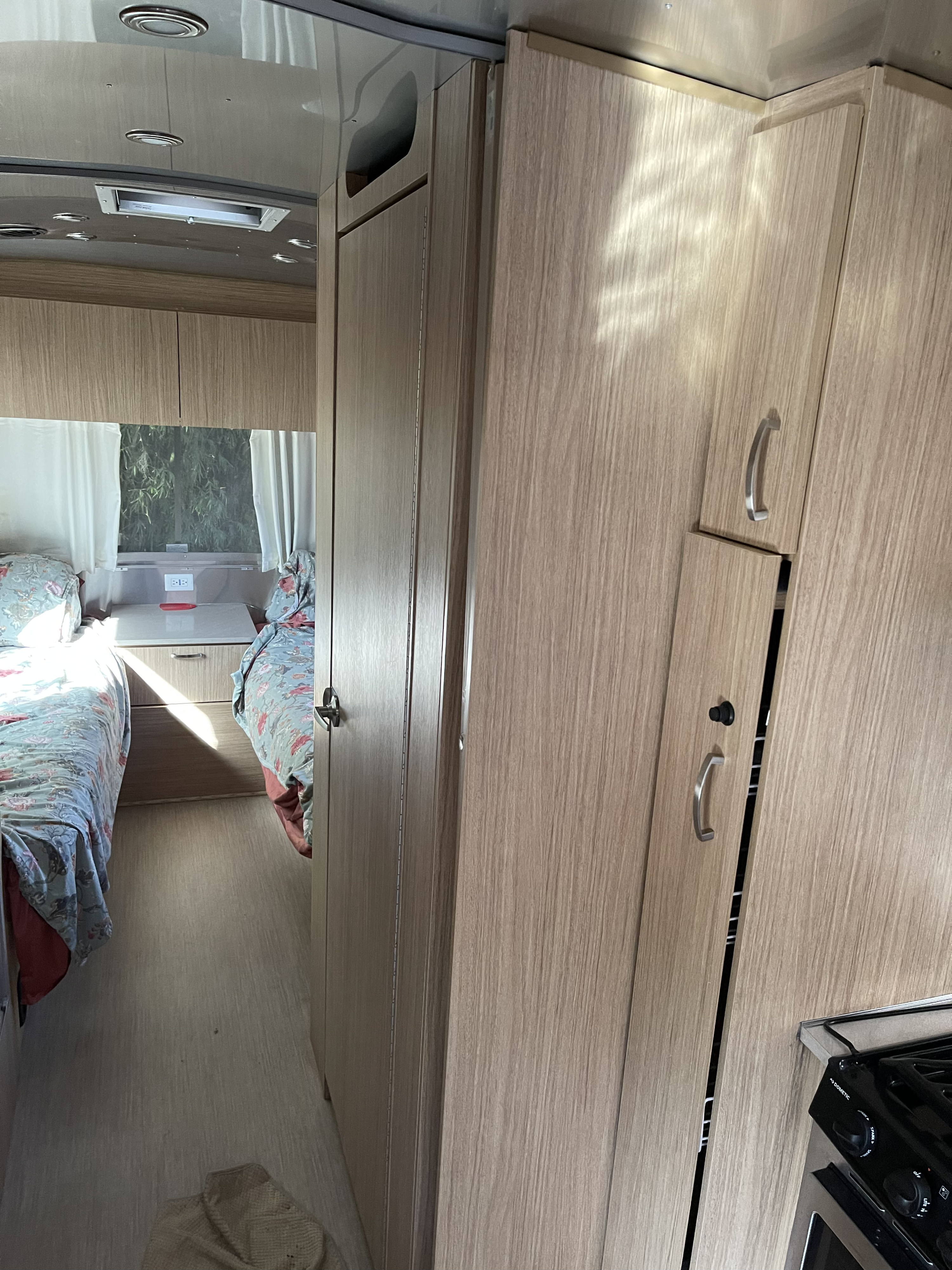 Interior of an RV rental showing a bedroom with floral bedding, light wood cabinets, and a partial kitchen.. Airstream Flying Cloud 2019