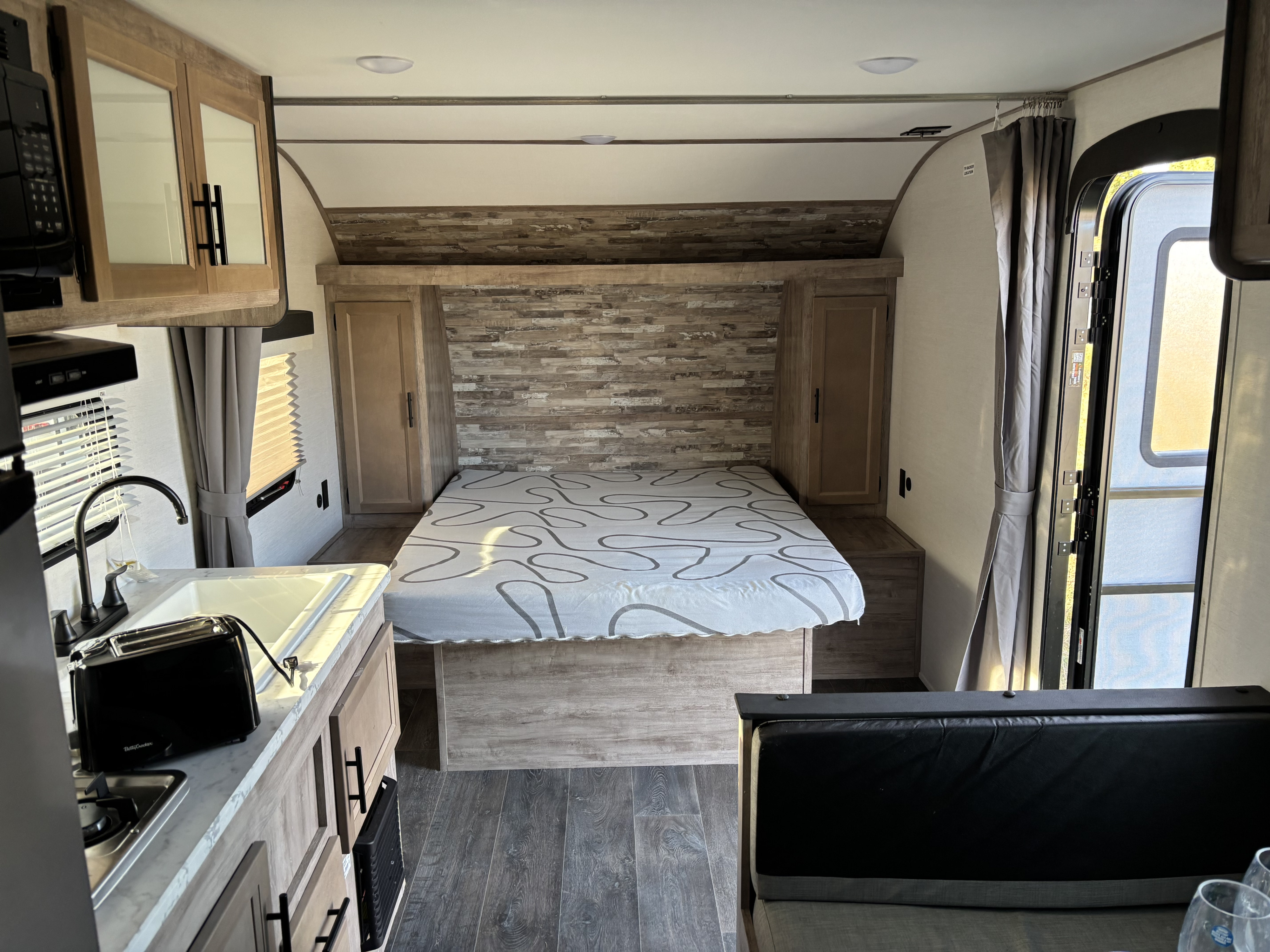 Experience an RV rental: compact kitchen, cozy bedroom with textured headboard, and dinette seating inside a travel trailer.. Forest River grand river 2024