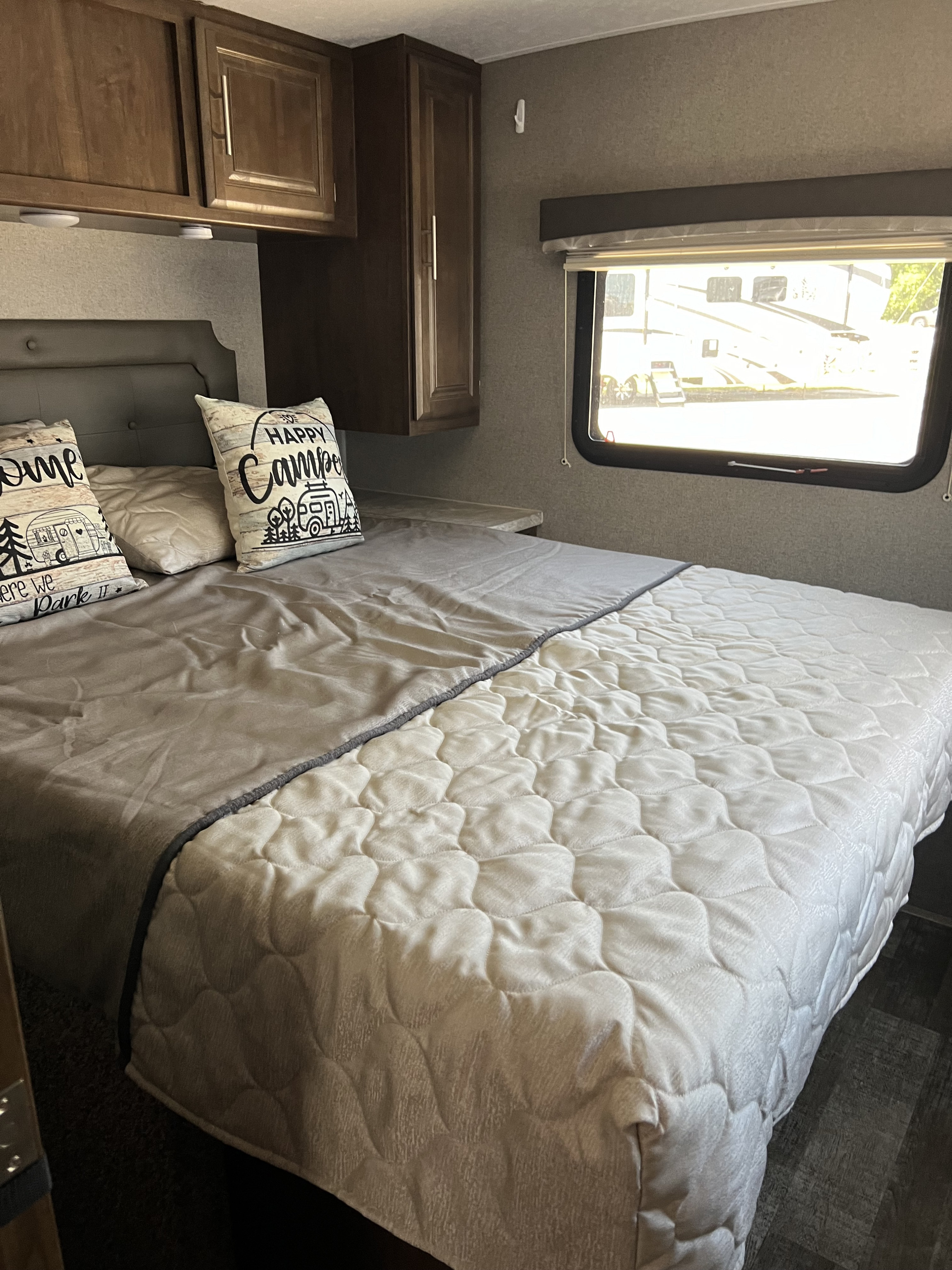 Cozy RV rental bedroom with a bed, "Happy Camper" pillows, wooden cabinets, and a bright window view.. Forest River Rockwood Mini Lite 2020