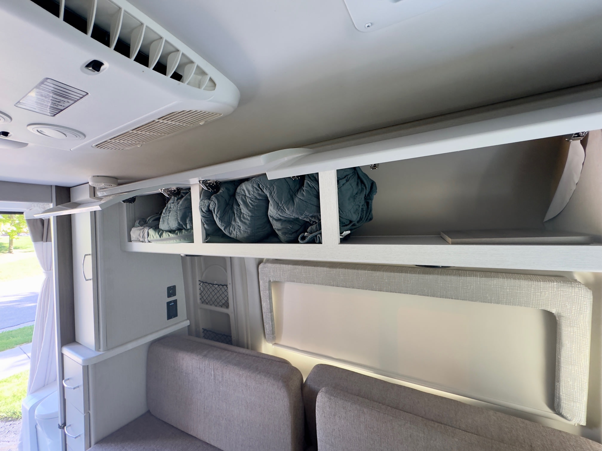 Glimpse inside an RV rental: ceiling AC, open storage with bedding, and light seating for comfortable travel.. Thor Rize 2022