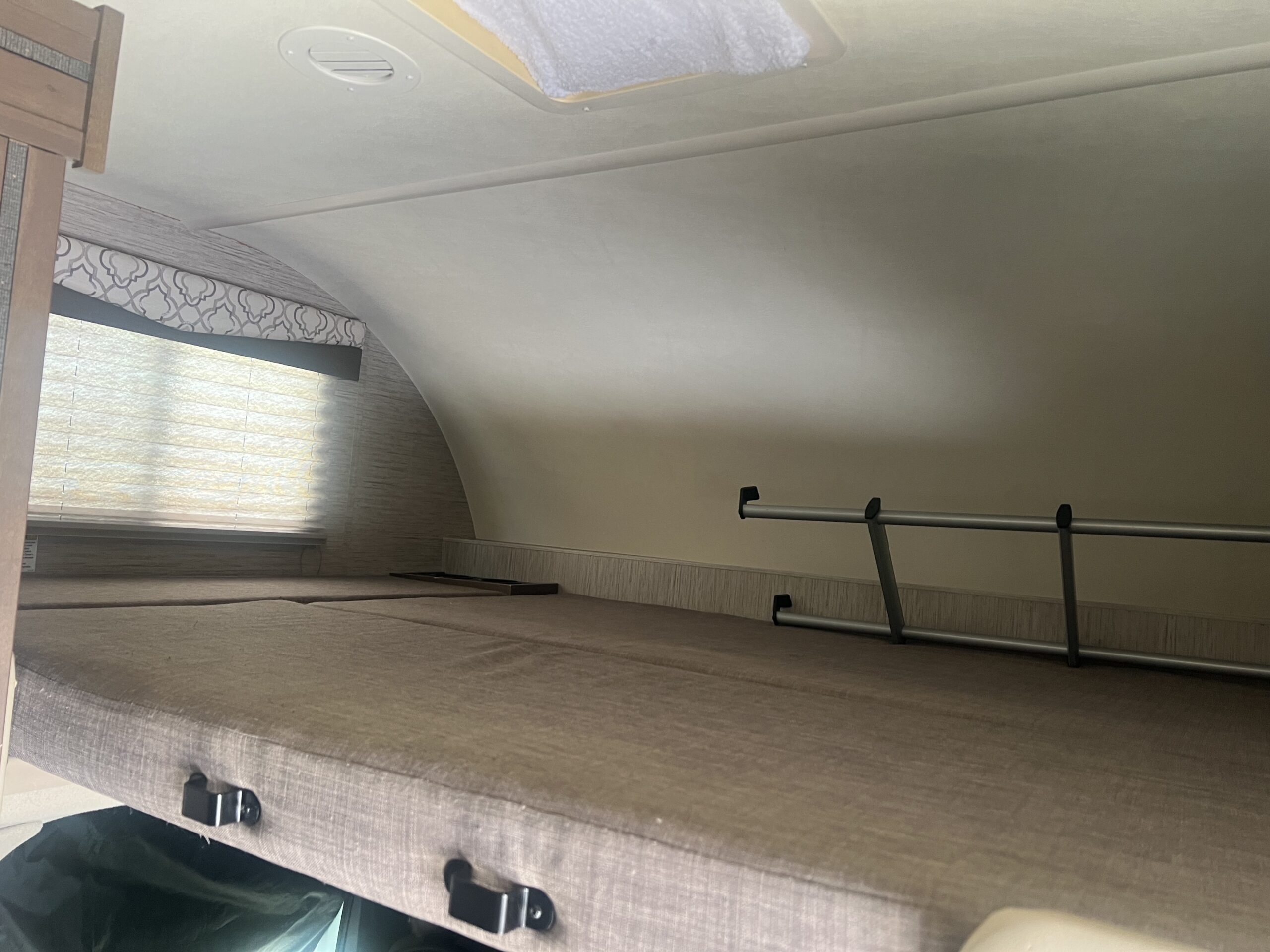 Inside an RV rental: a cozy bunk bed with a ladder, window blinds, and an overhead vent on the ceiling.. Thor Freedom Elite 2021