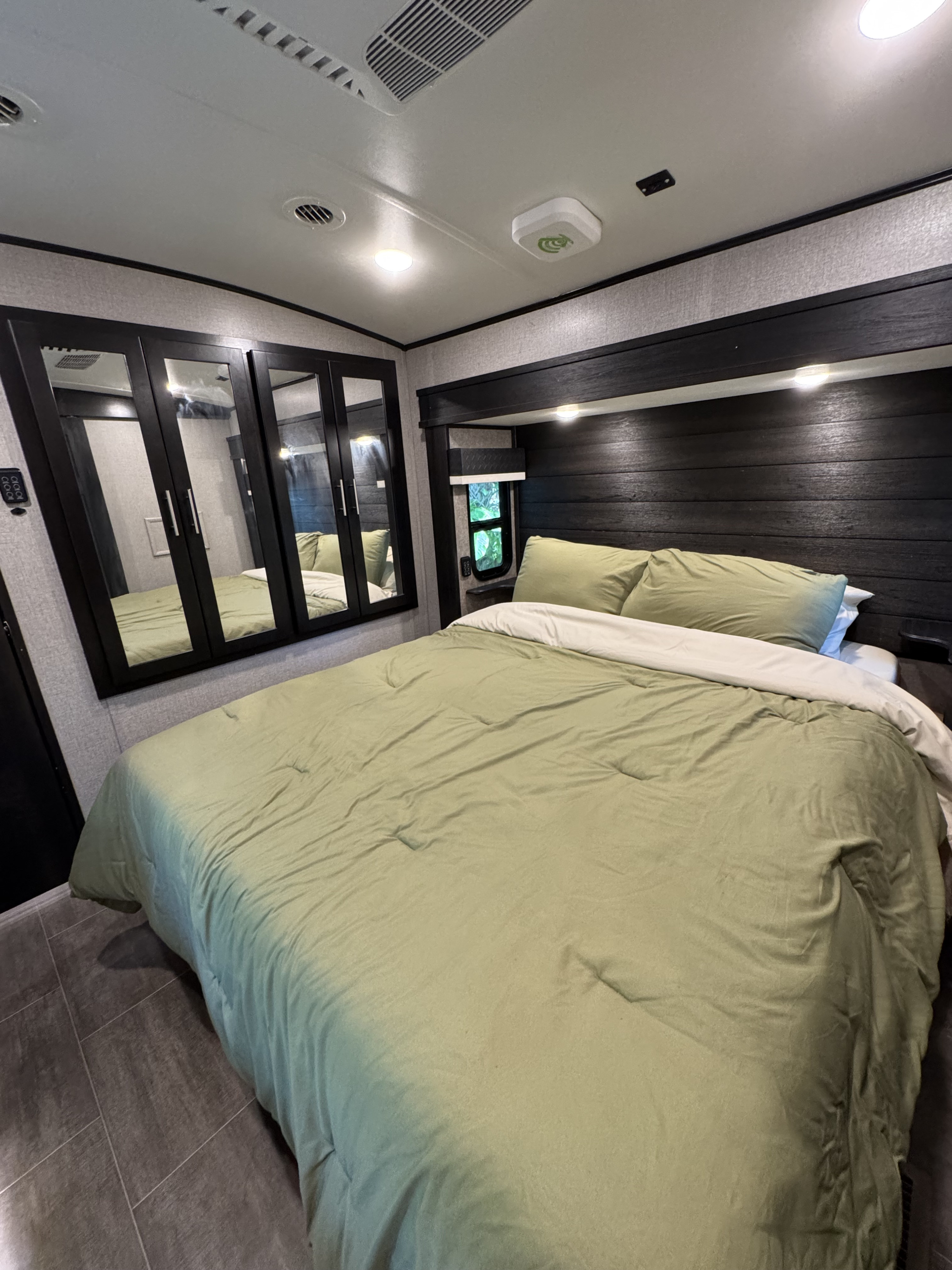 This RV rental bedroom features a comfy bed with green sheets, a sleek dark wood headboard, and mirrored wardrobe doors.. Jayco North Point 2020