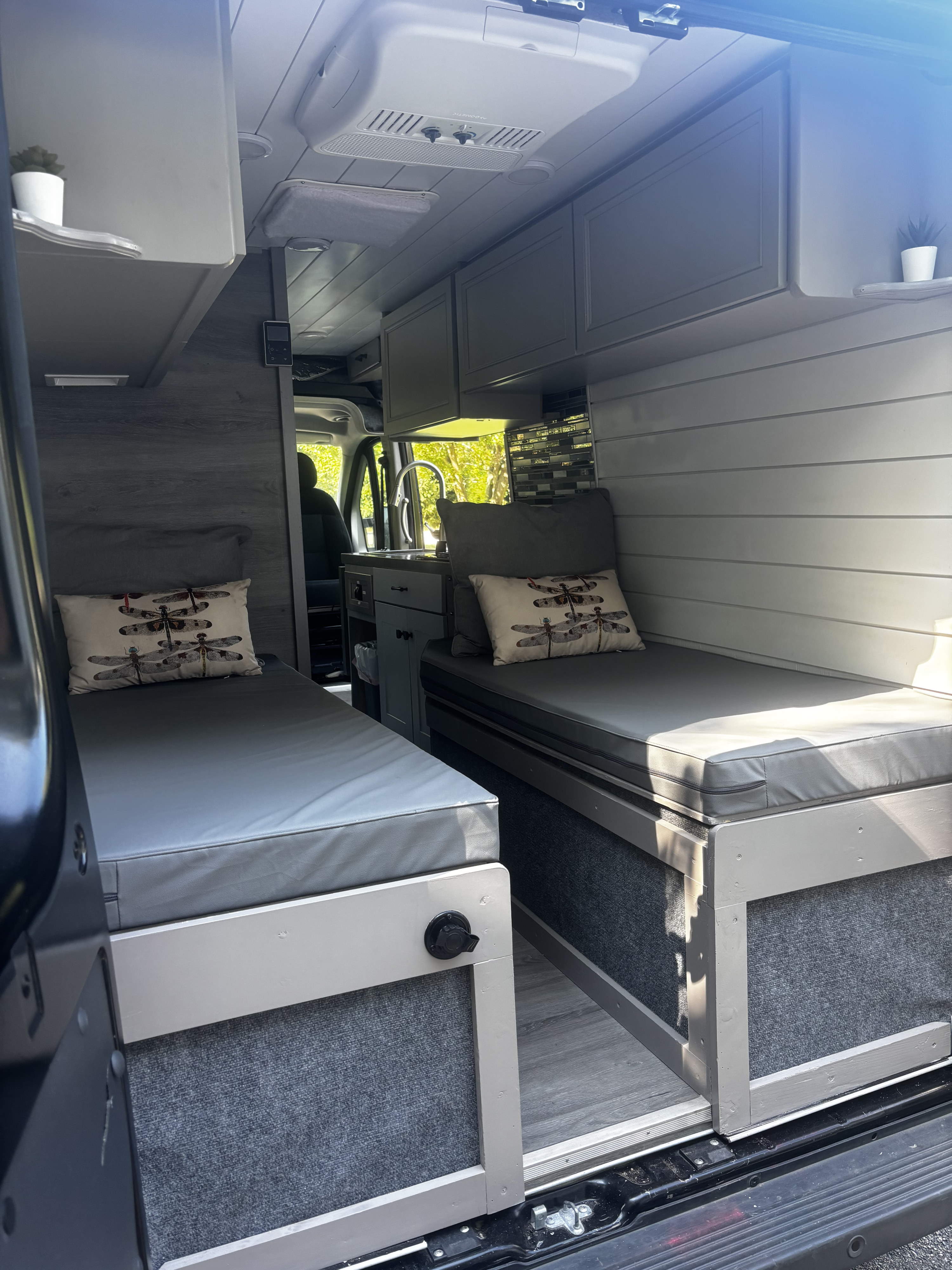 Cozy RV rental interior with twin beds, gray cushions, overhead storage, a compact kitchen, and ceiling AC unit.. Ram Promaster 2500 High Roof 2016