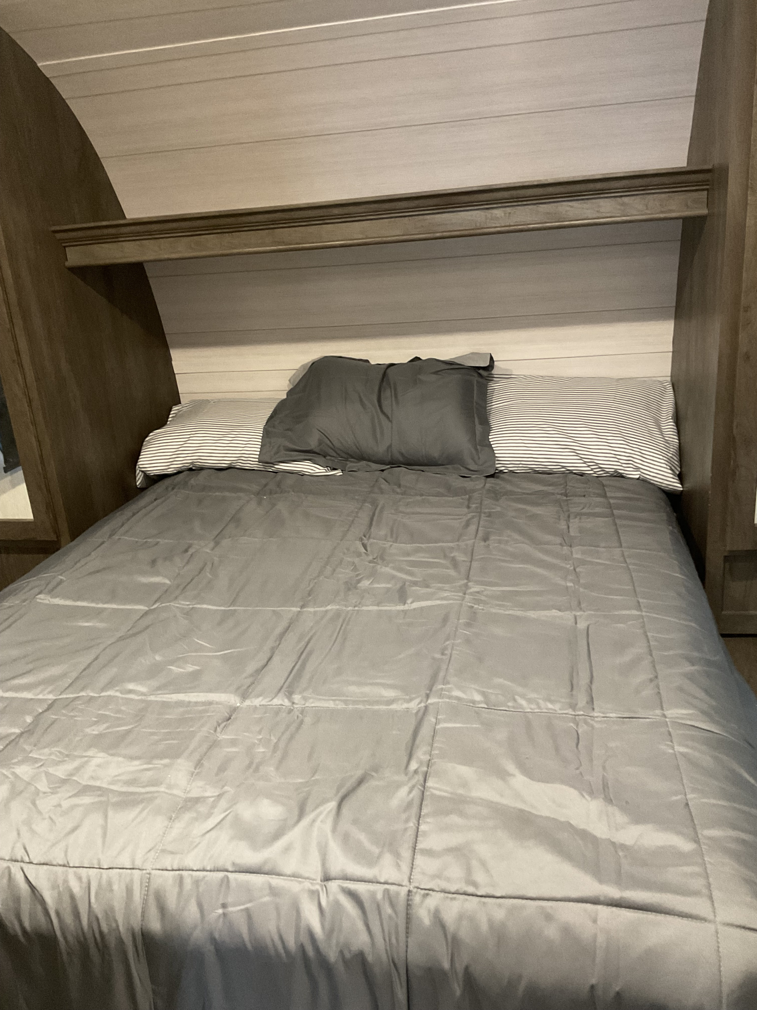 RV rental bedroom: a cozy sleeping area with gray bedding, striped pillows, and wood paneling.. Forest River Shockwave 2022