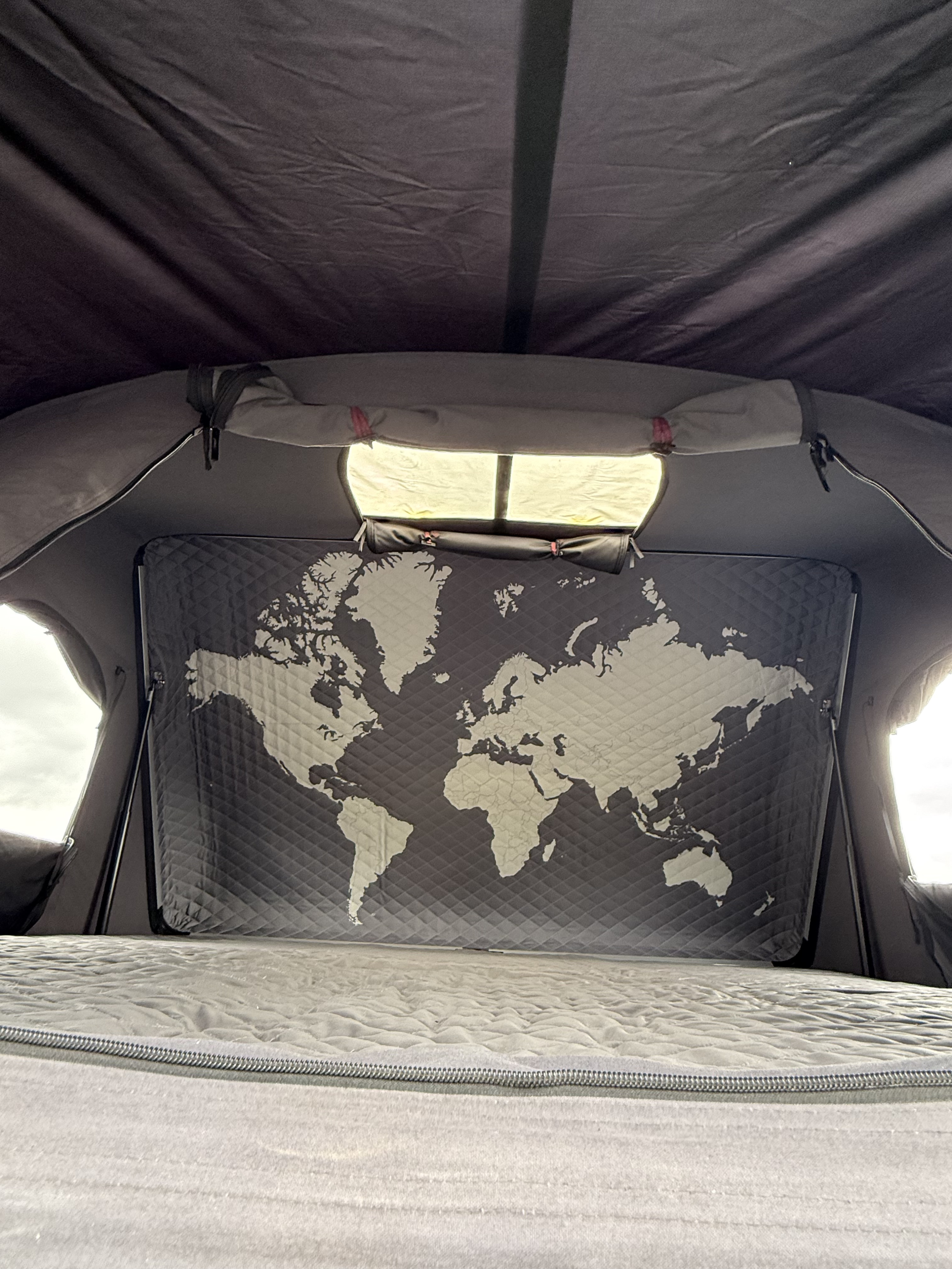 Cozy RV rental interior with a bed & quilted world map panel, illuminated by side and top windows.. Toyota Tundra 2025