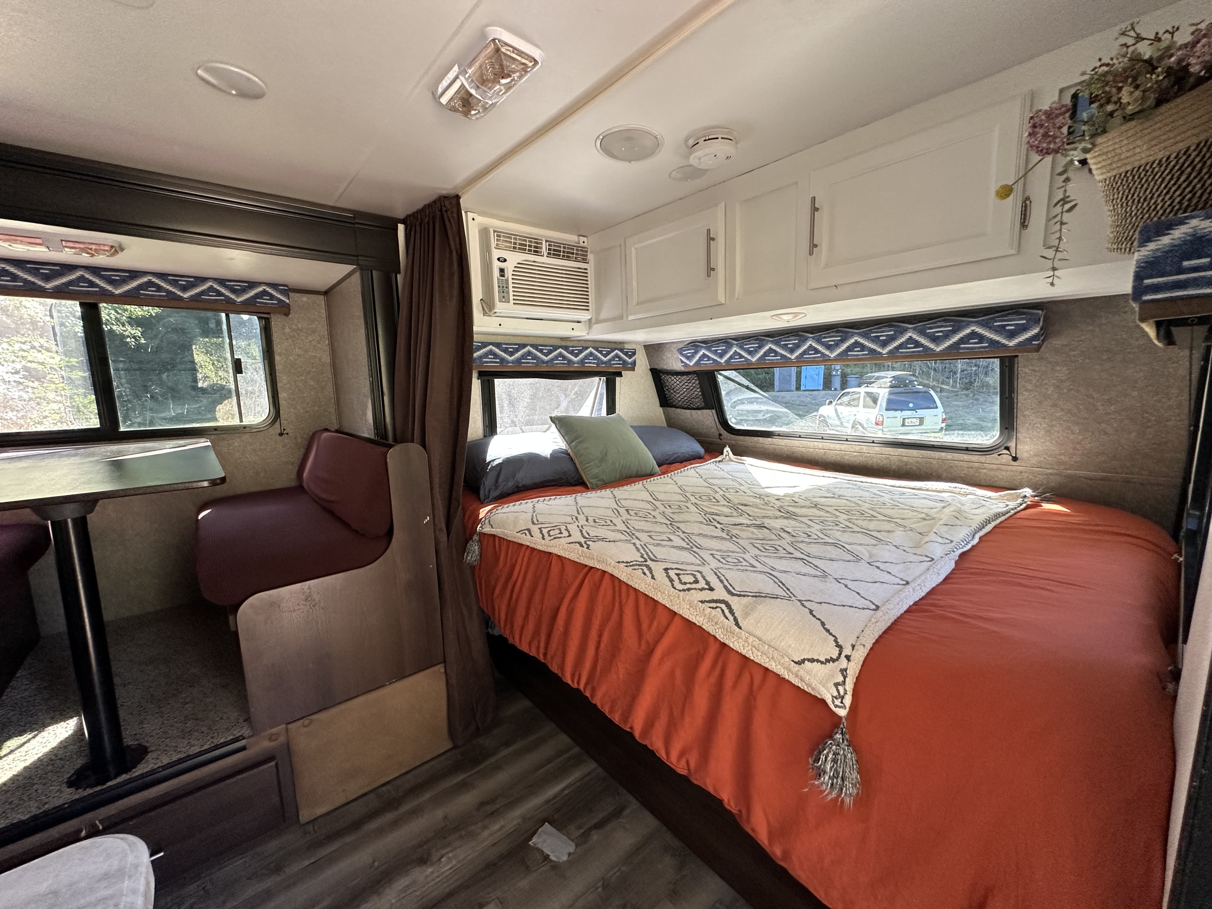 RV rental interior: cozy bedroom with orange bedding, patterned blanket, and dining area. Enjoy the view from the window!. Jayco Jay Flight SLX Baja Edition 2019