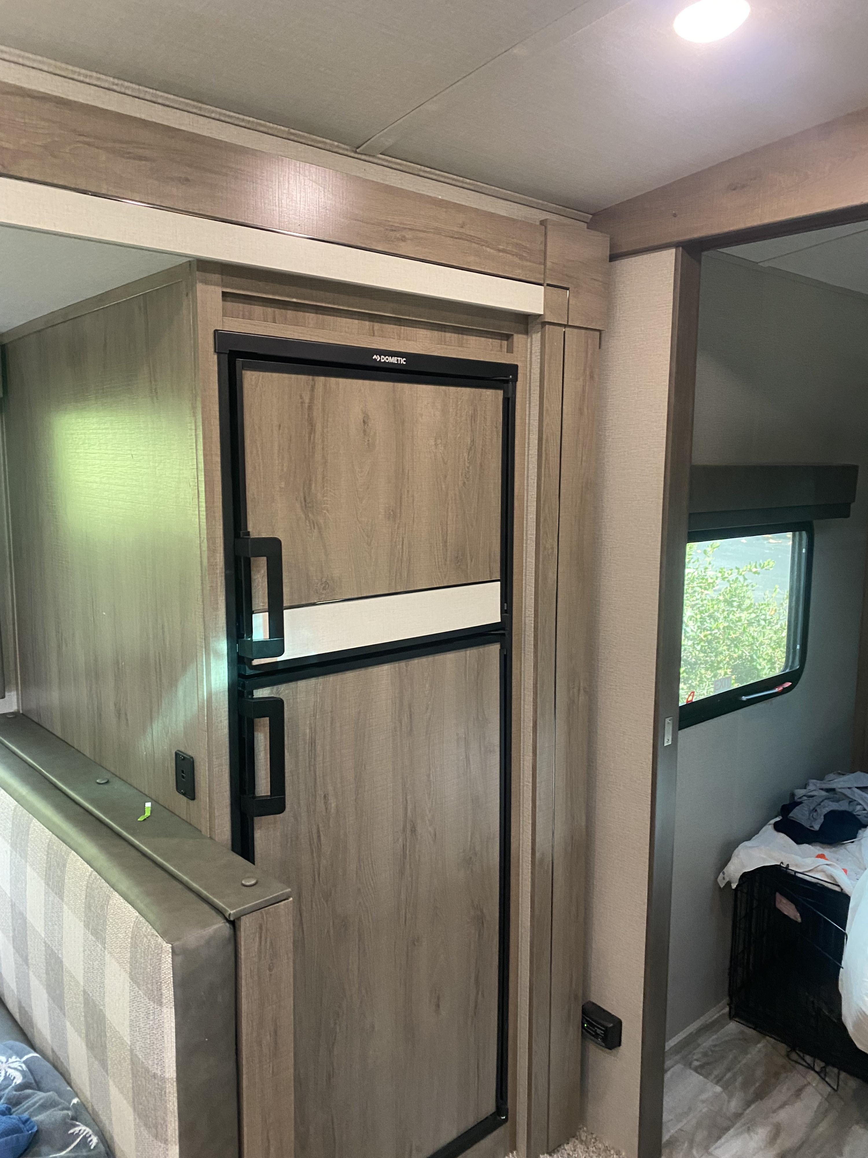 Inside an RV rental: a Dometic refrigerator with wood-look panels, a plaid upholstered bench, and a window. Perfect for travel adventures.. Grand Design Imagine 2022