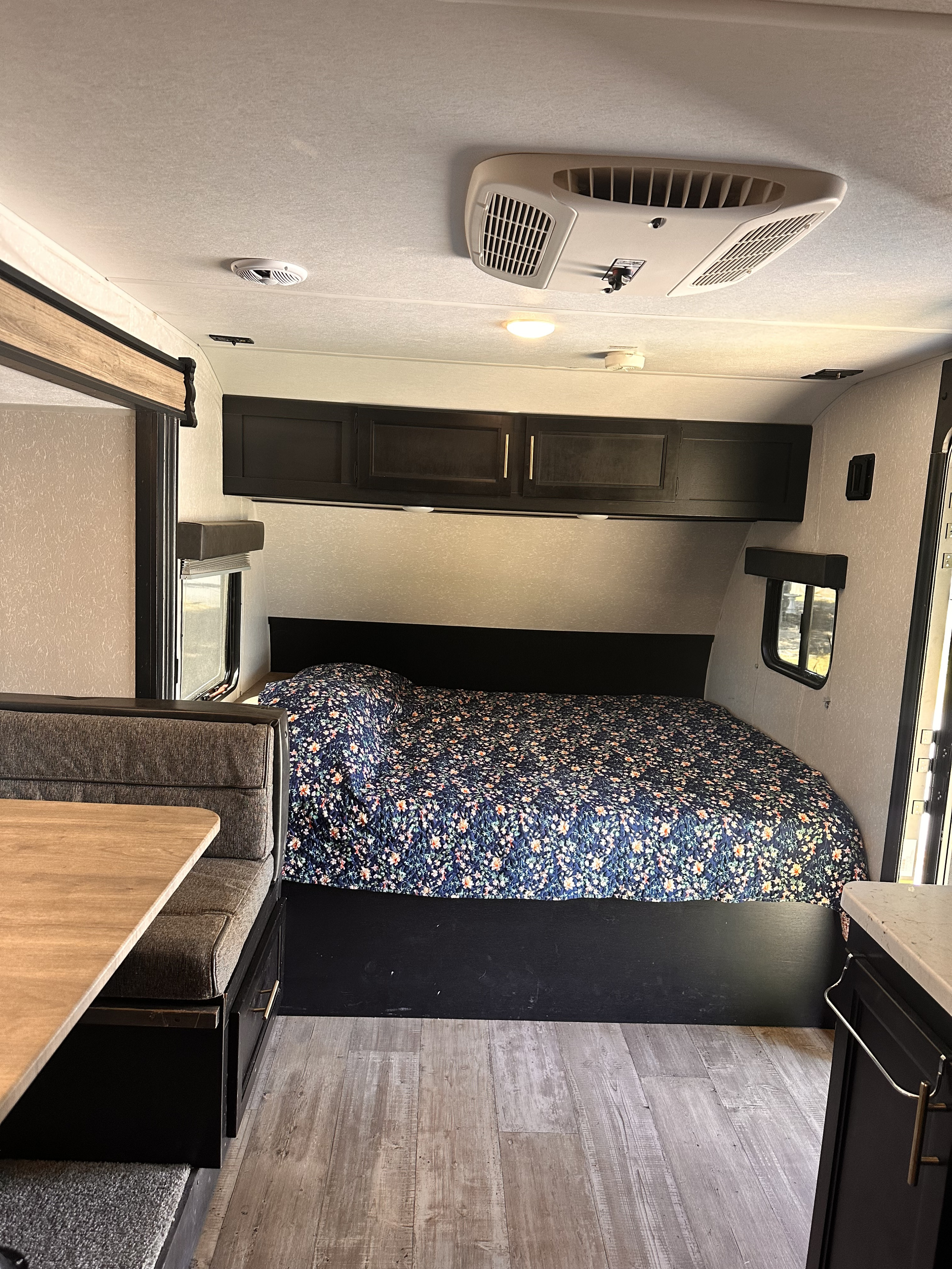 Cozy RV rental interior featuring a comfortable bed with a floral comforter, dinette, and overhead storage.. Forest River Cherokee Wolf Pup 2021