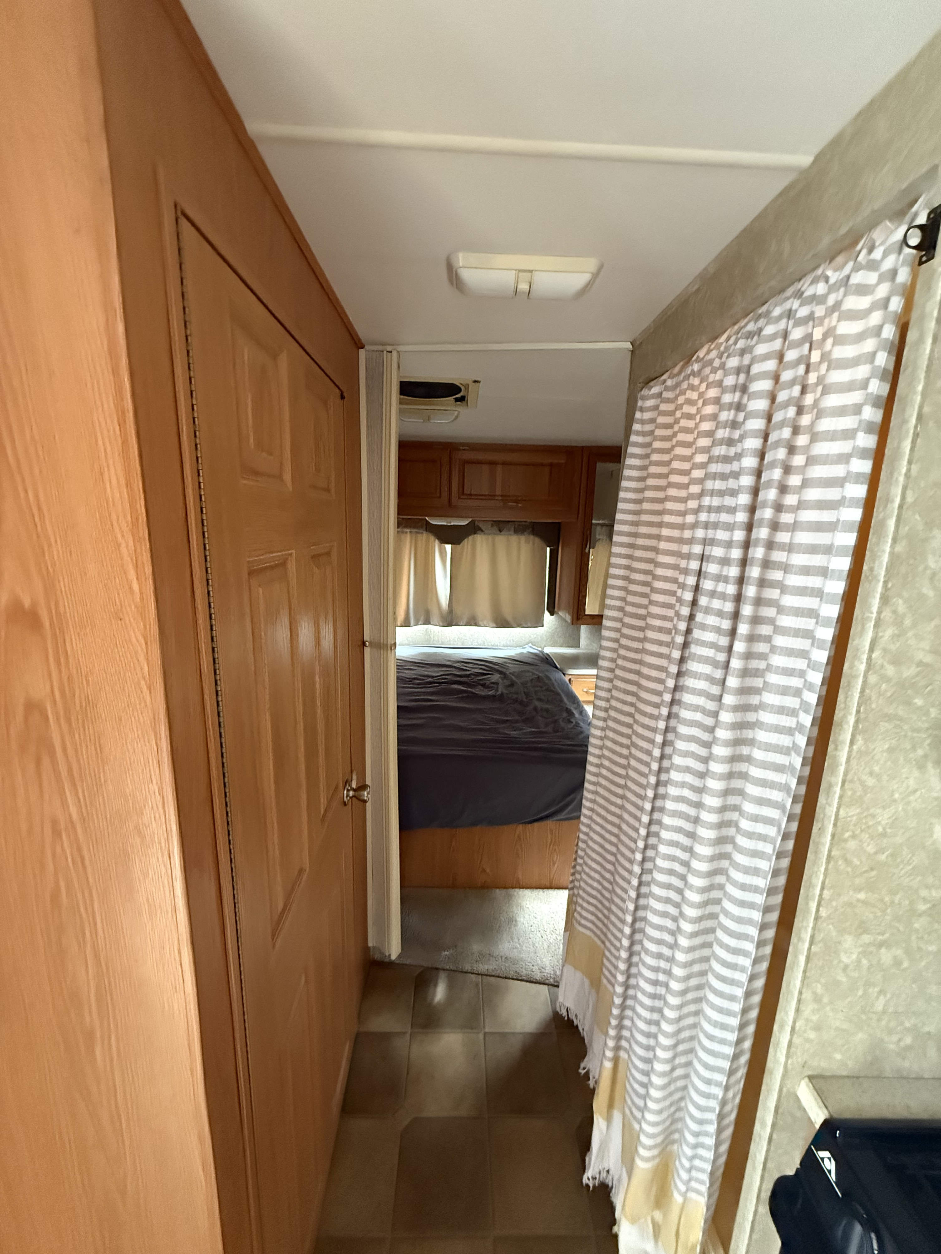 Inside an RV rental, a hallway leads to the bedroom with a dark bed, cabinetry, and a striped privacy curtain.. Four Winds 5000 2005