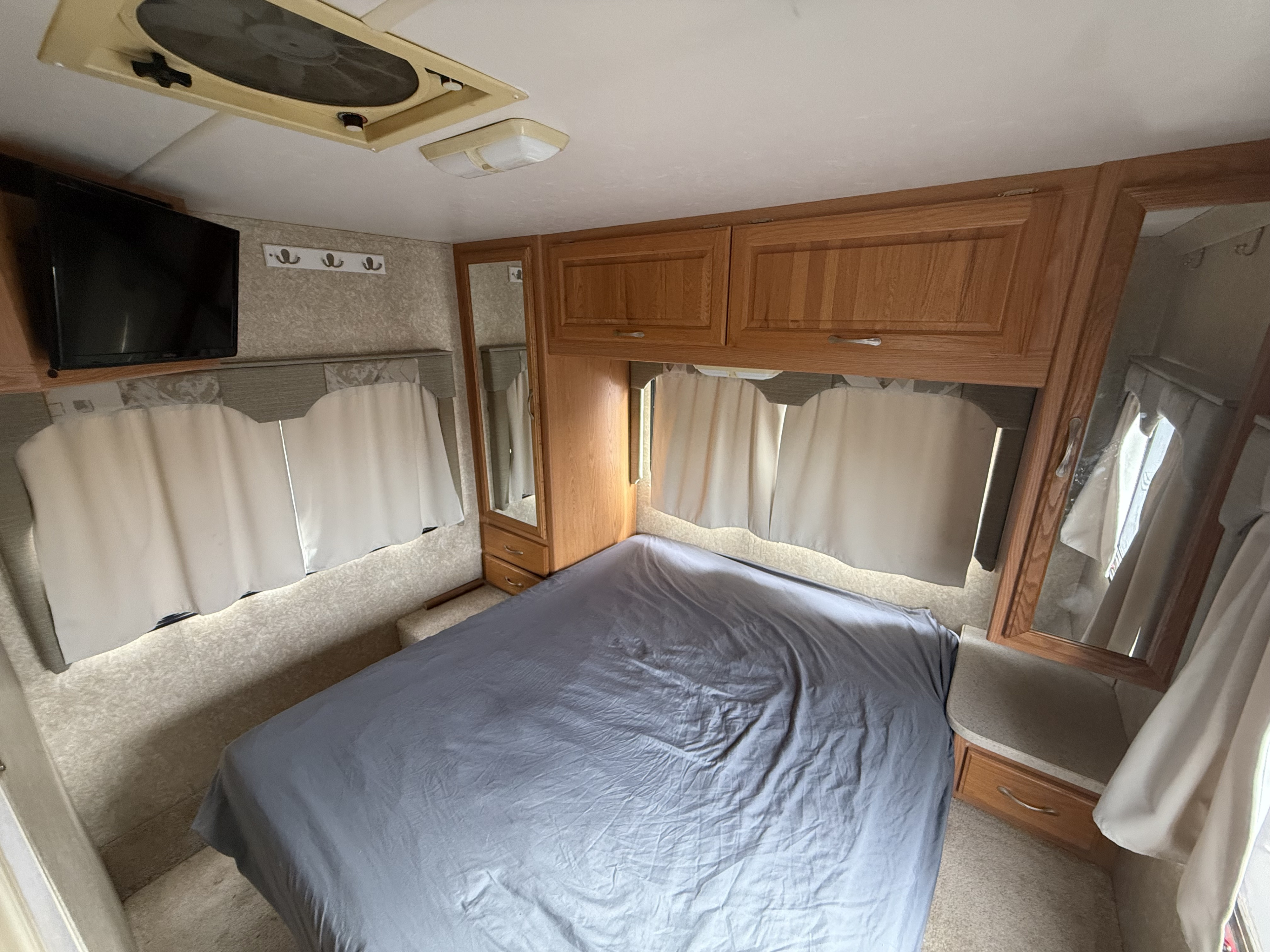 Cozy RV rental bedroom featuring a grey bed, wooden cabinets, TV, and ceiling fan. Ideal for travel.. Four Winds 5000 2005
