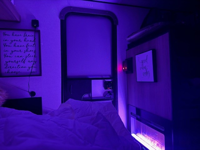 Cozy rv rental interior: purple light, comfy bed, electric fireplace, and inspiring quotes create a relaxing bedroom vibe.. Colman 13B 2025