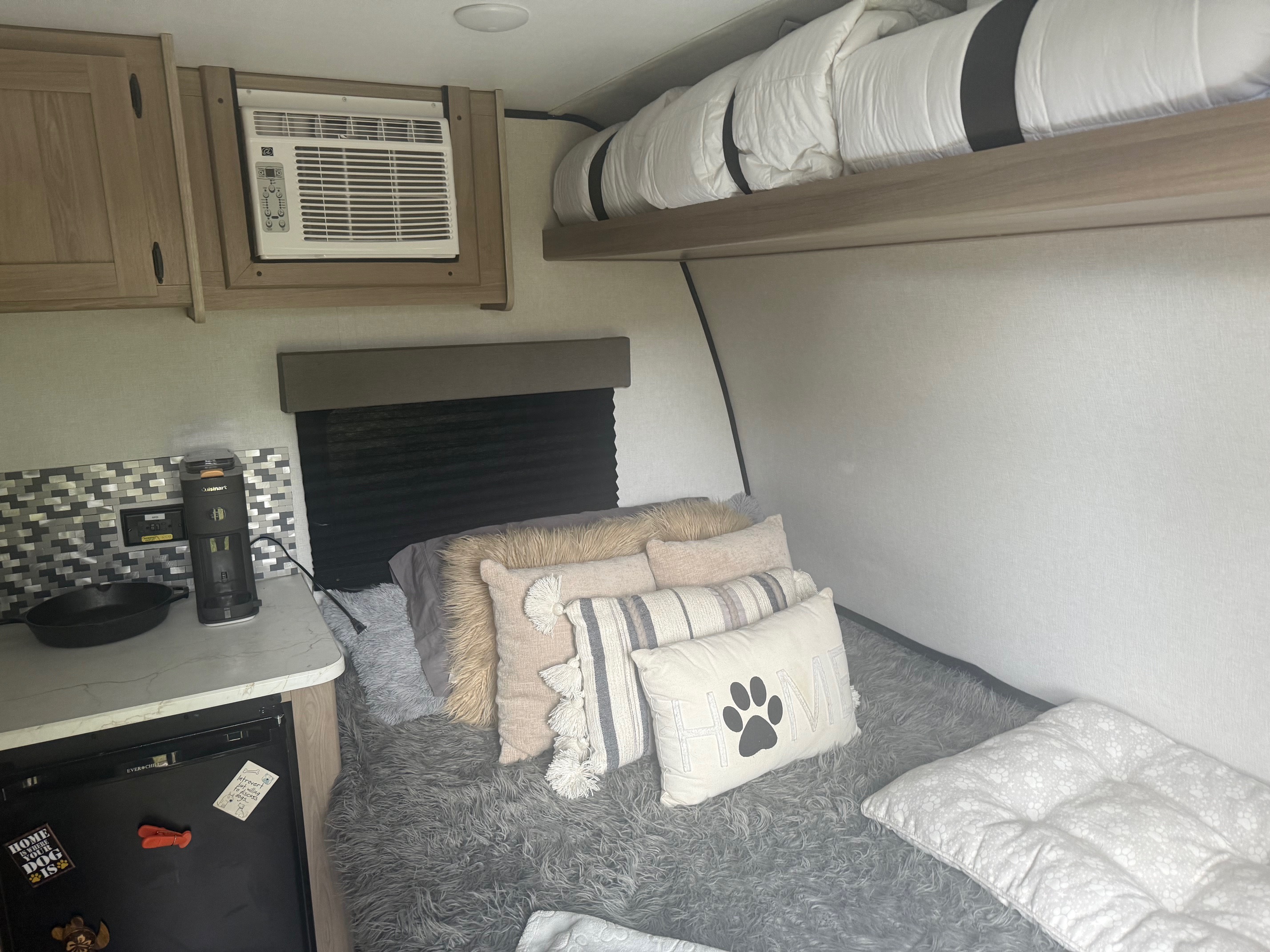 Cozy RV rental interior with a dog-friendly sleeping area, kitchenette, AC unit, and overhead bunk bed. Compact & inviting.. Colman 13B 2025