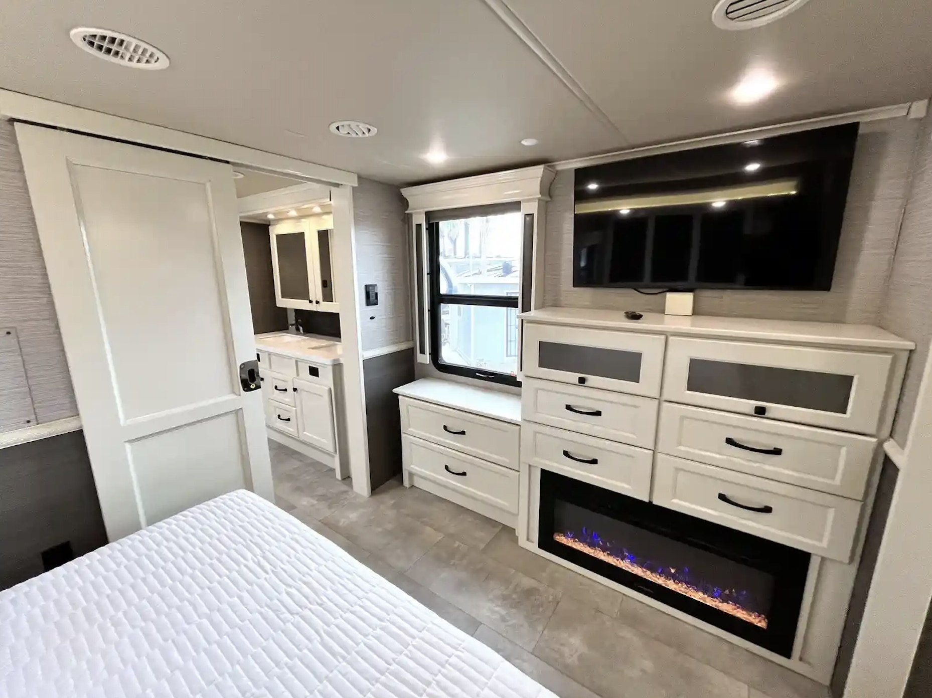 Spacious RV rental bedroom with a cozy bed, TV, fireplace, and a sliding door leading to the modern bathroom.. Vanleigh RV Beacon 2022