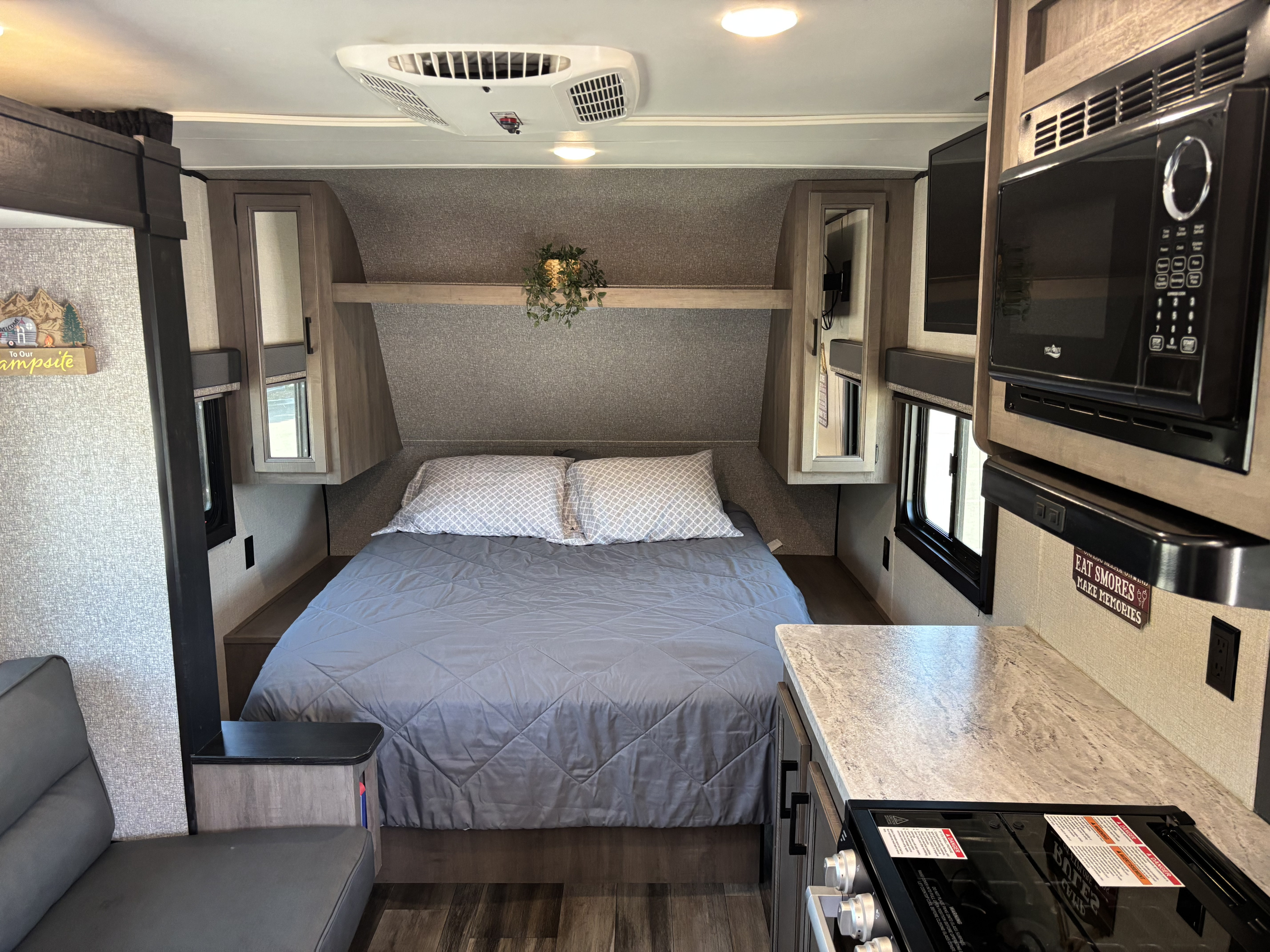 Cozy RV rental interior showing a bed with gray bedding and a compact kitchen area with a microwave and stovetop.. Starcraft Autumn Ridge 2022