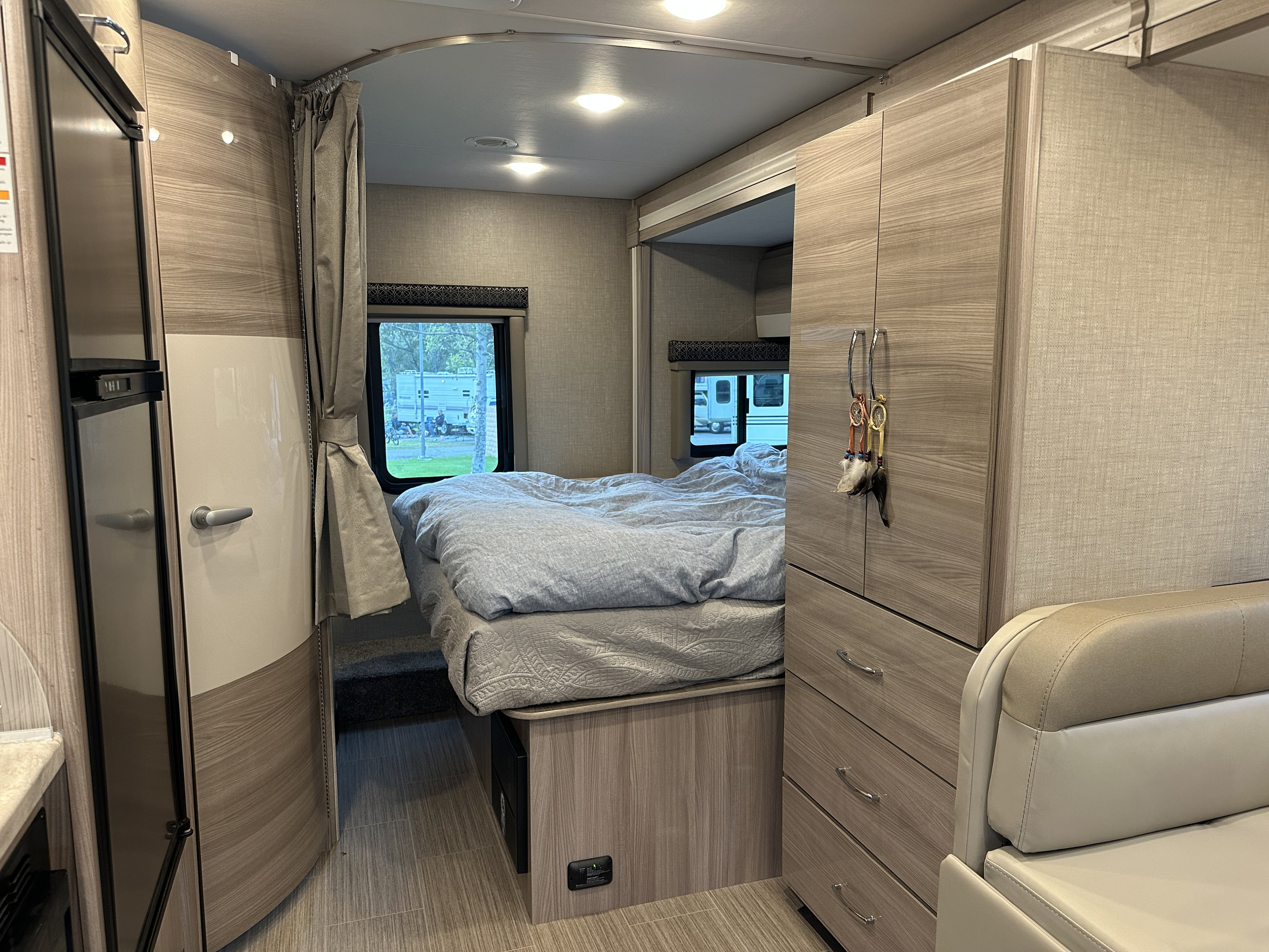 Comfortable RV rental bedroom featuring a light wood interior, bed, window, and storage cabinets.. Thor Tiburon SV 2023