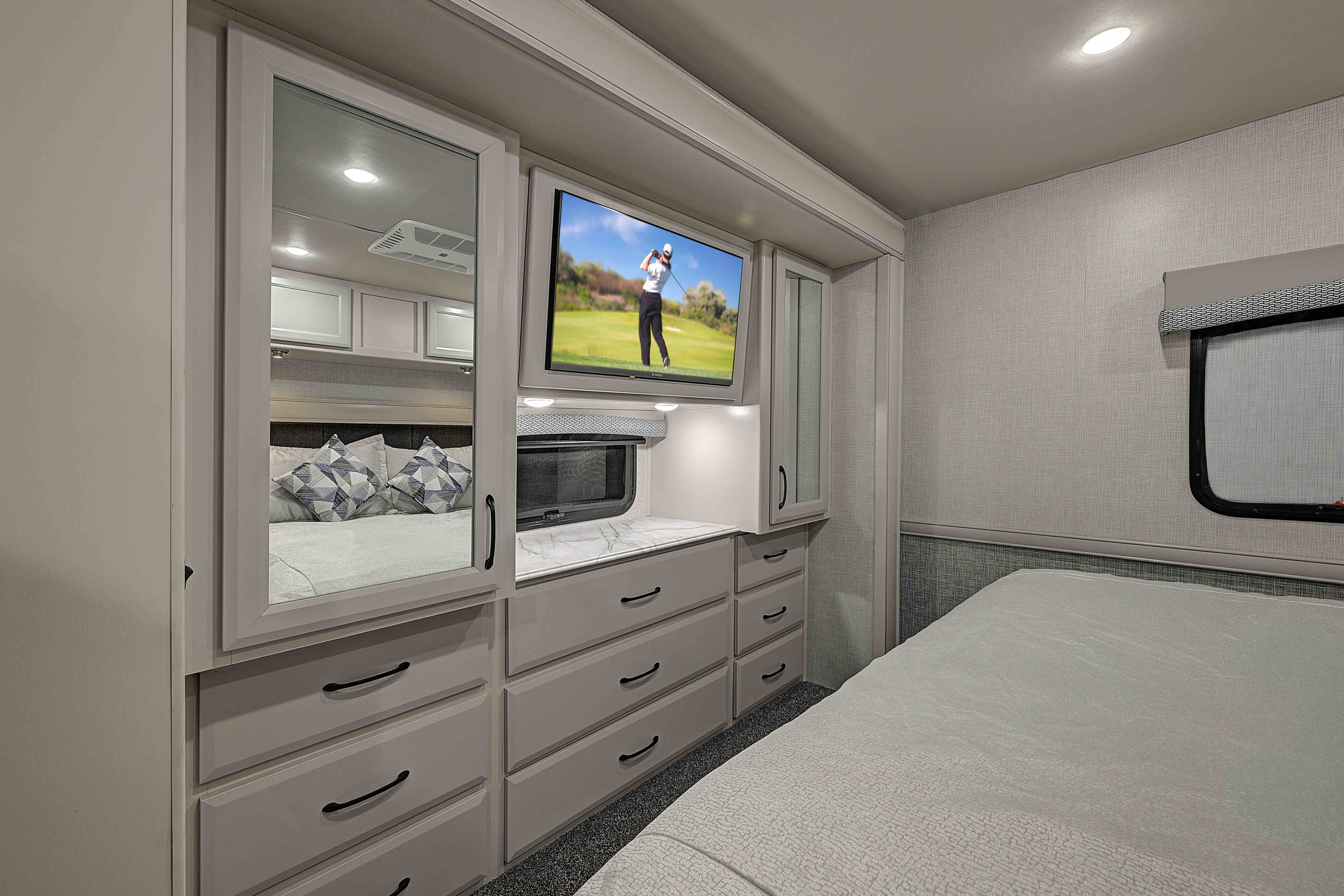Modern RV rental bedroom featuring built-in dresser, TV, mirrored wardrobe, bed, and window for comfortable travel.. Fleetwood Flair 2025