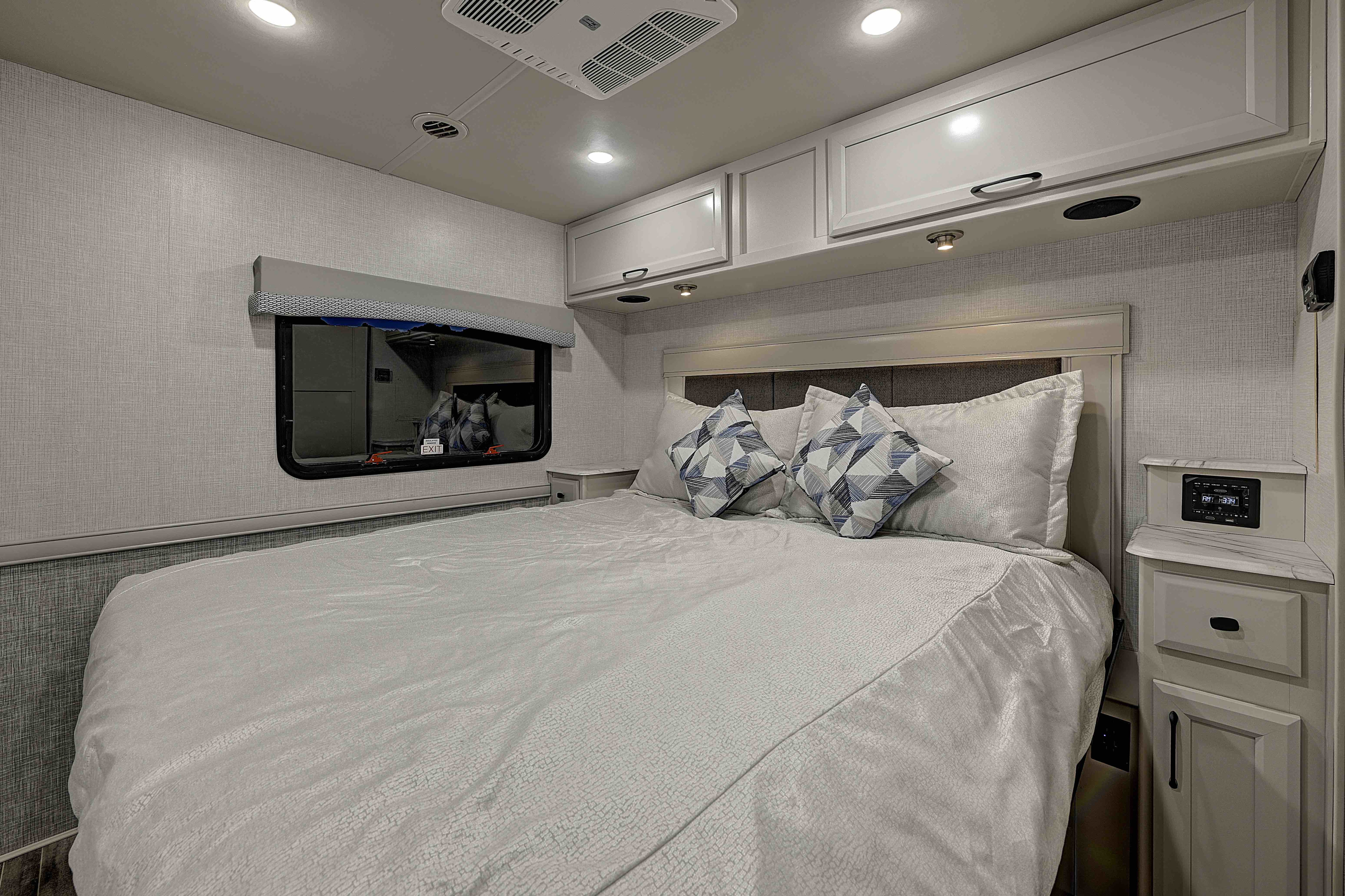 Relaxing RV rental bedroom features a comfortable bed with decorative pillows, overhead storage, and a handy bedside control panel.. Fleetwood Flair 2025