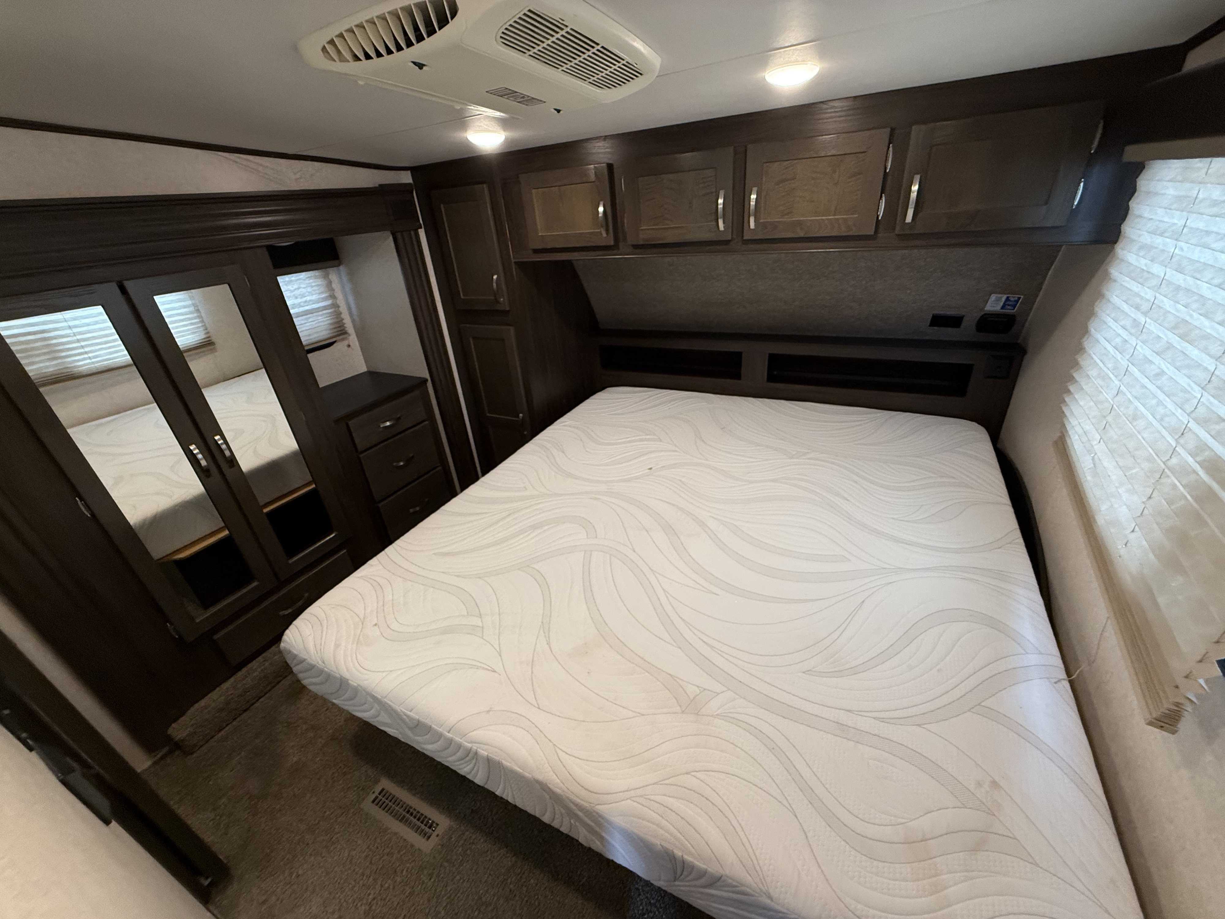 Spacious RV rental bedroom features a comfortable bed, overhead storage, mirrored wardrobe, and AC unit for your travels.. Jayco Octane 2019