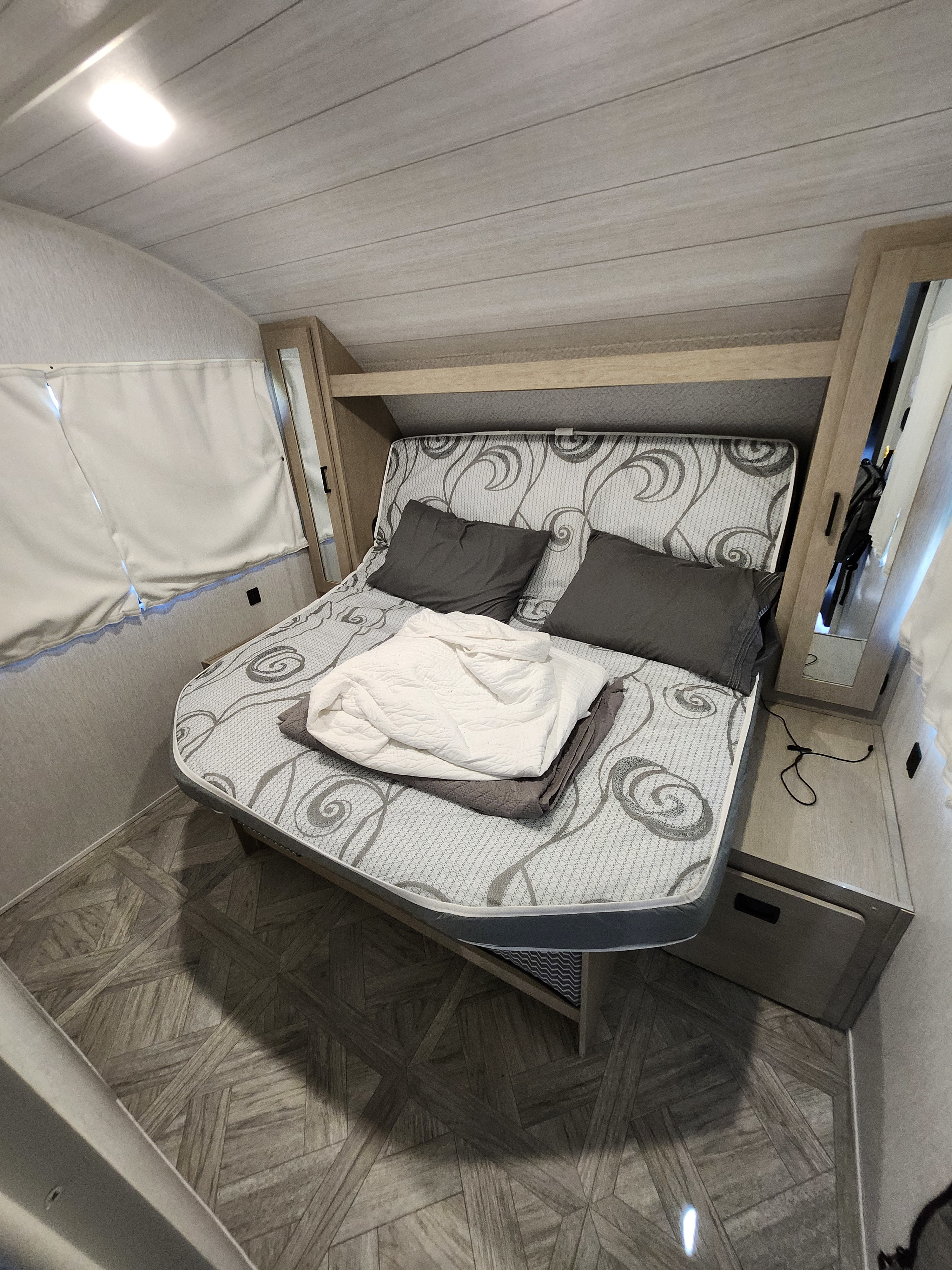 Cozy rv rental bedroom: a bed with gray pillows, light wood mirrored cabinets, planked ceiling, and geometric wood-look floor.. Forest River Salem Cruise Lite Platinum 2024