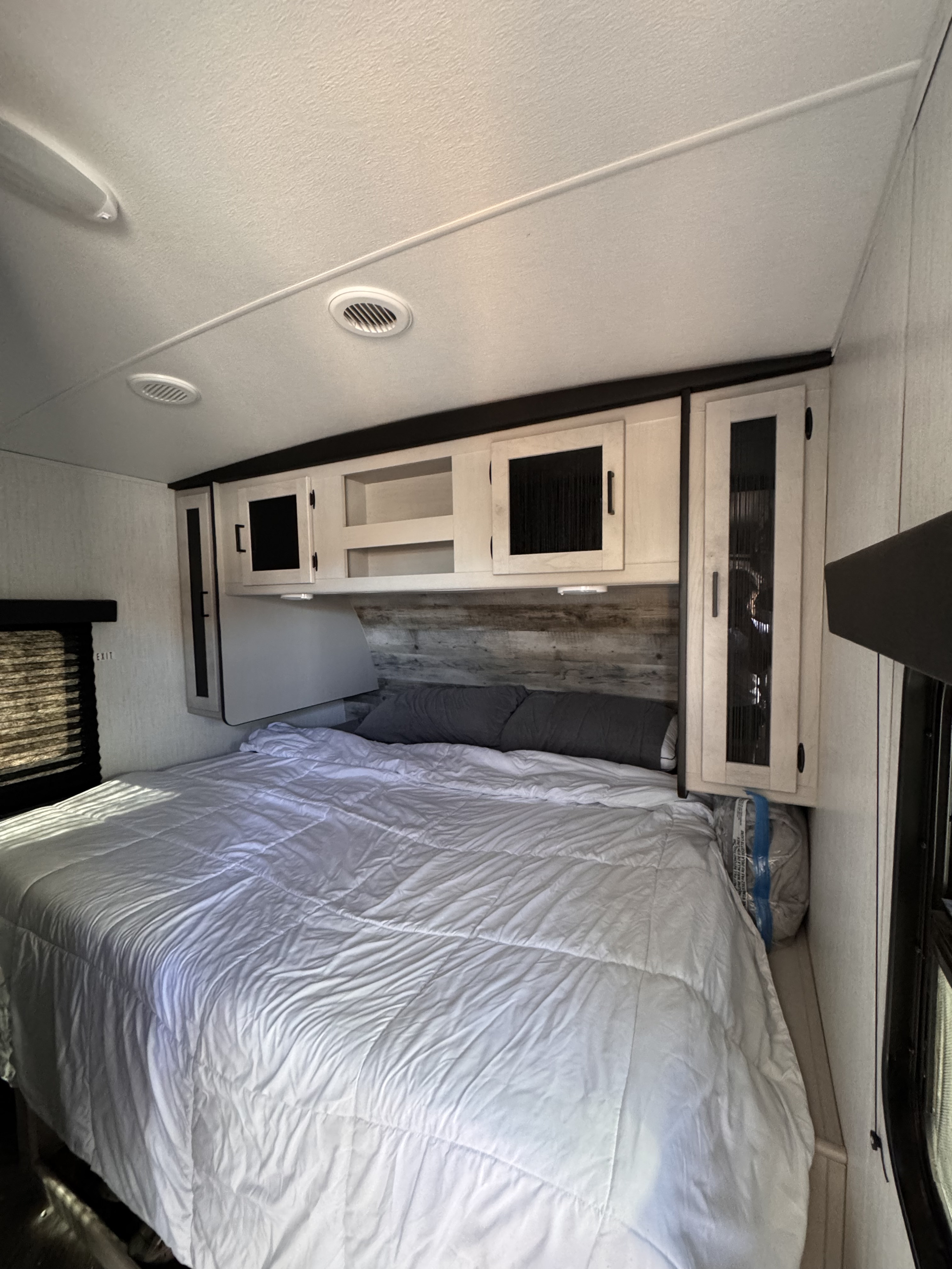Comfortable RV rental bedroom with a large bed, white bedding, grey pillows, and functional overhead storage.. Heartland RVs Mallard 2023