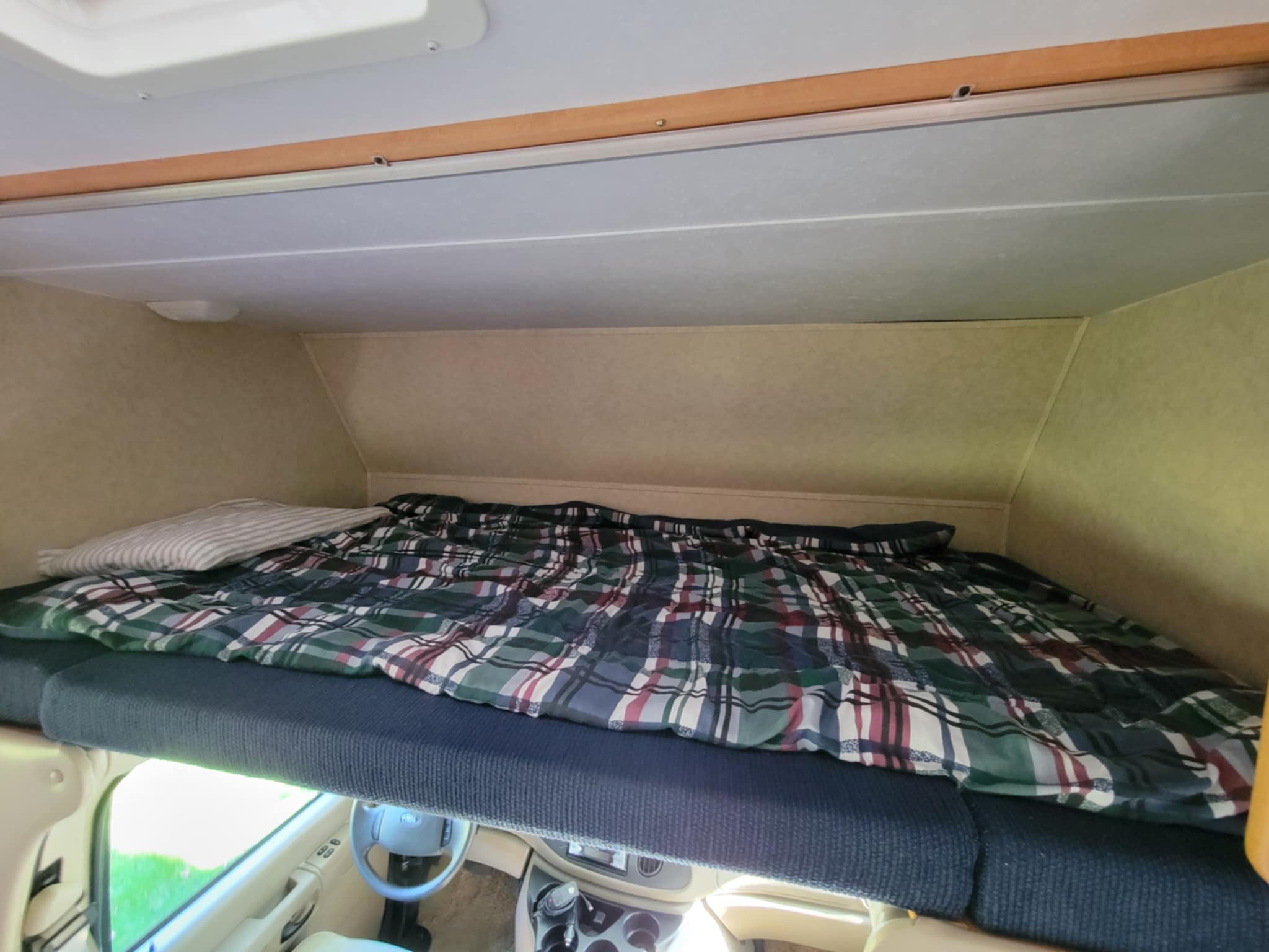 Cozy overhead sleeping area in an RV rental, with a plaid comforter. Great for comfortable travel above the cab.. Forest River Sunseeker LE 2006